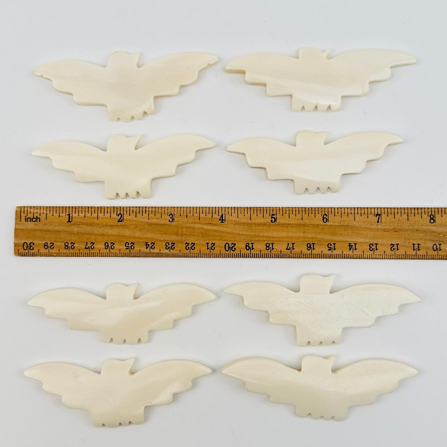 carved bone bats displayed next to a ruler for size reference 