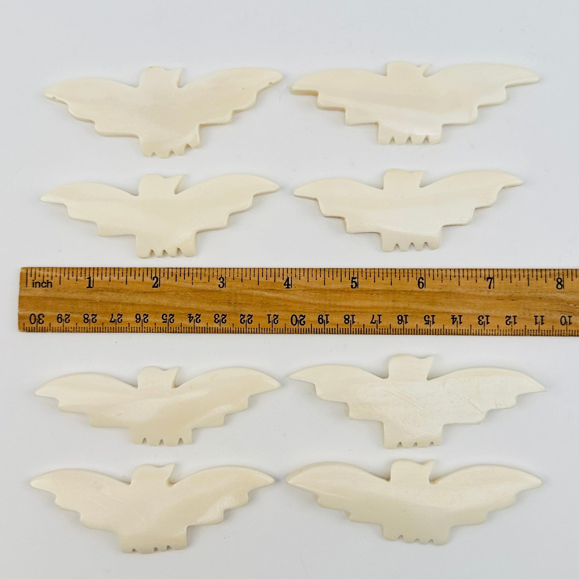 carved bone bats displayed next to a ruler for size reference 