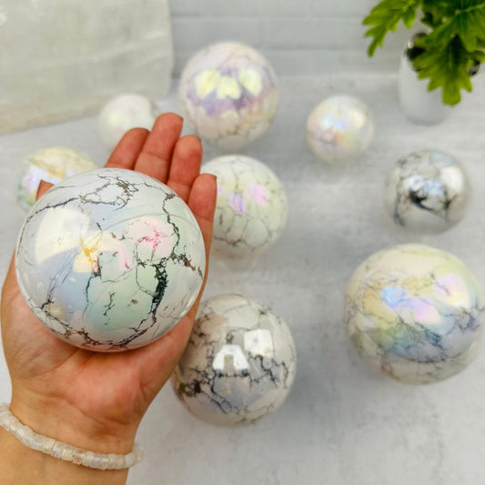 White Howlite Angel Aura Polished Sphere in hand for size reference 