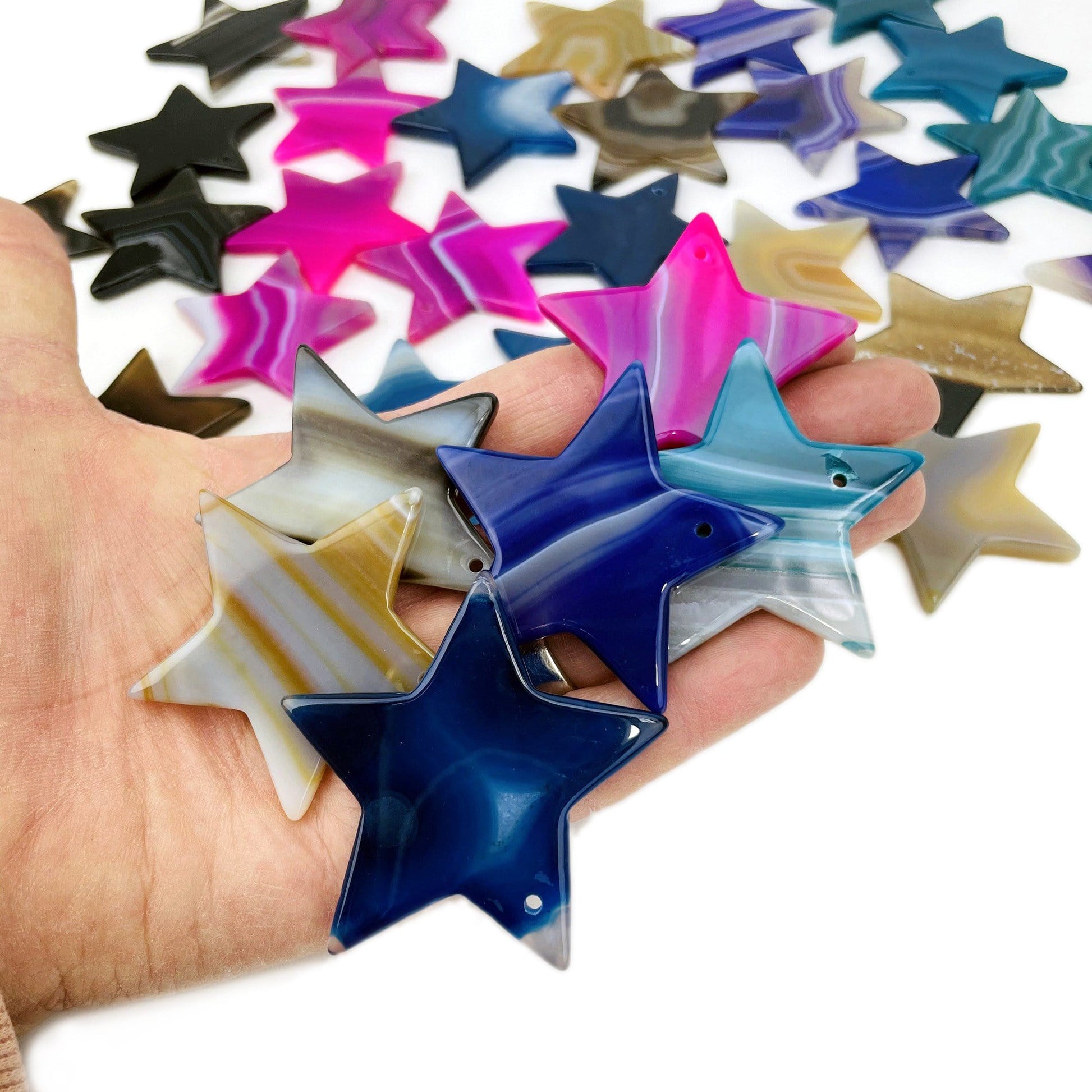 Assorted Color Drilled Agate Stars in Hand on White Background.