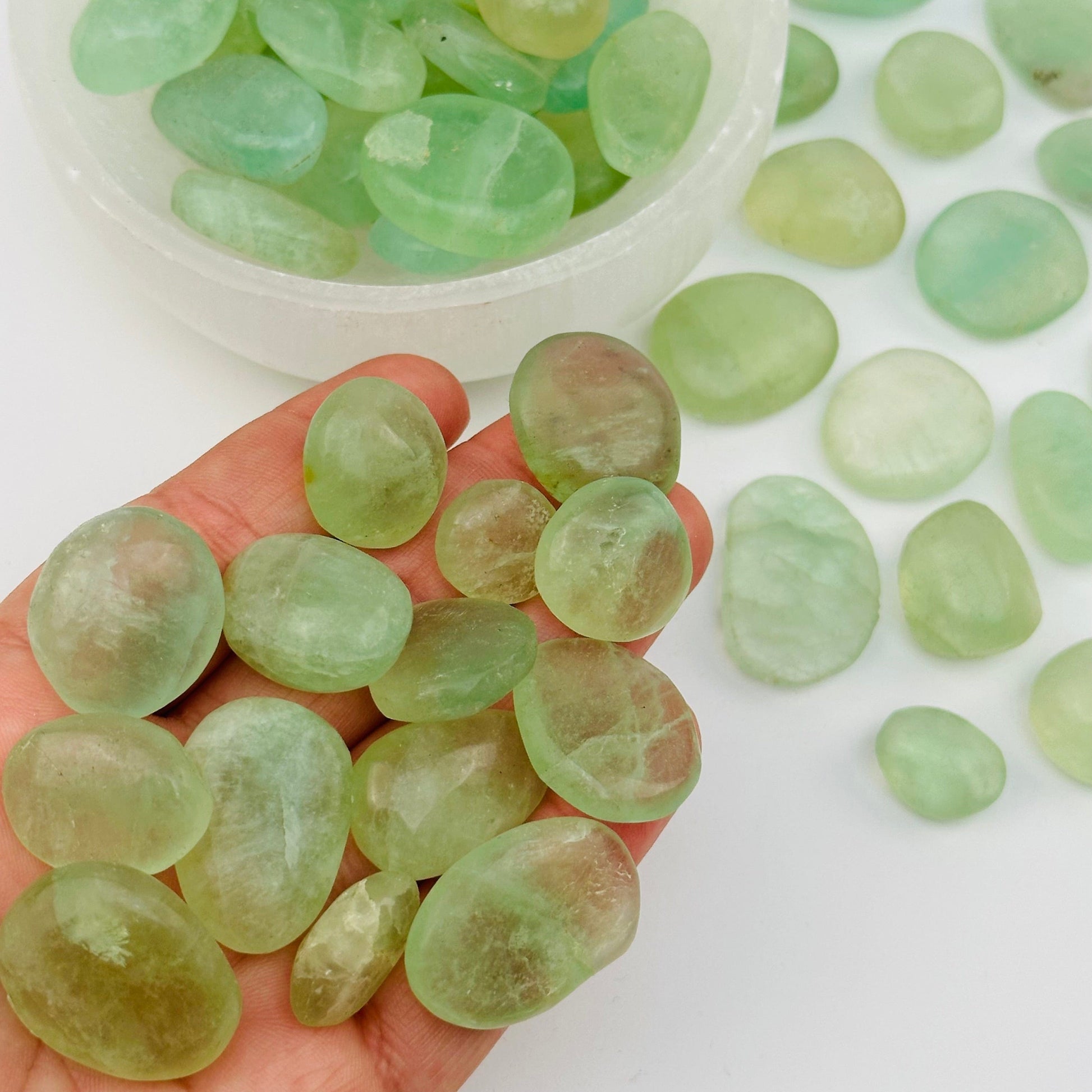 multiple tumbled fluorite stones in hand for size reference 