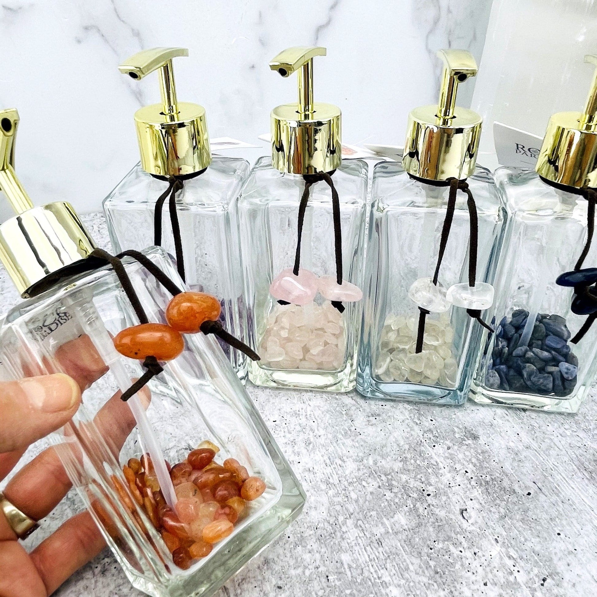 Tumbled Stone Soap Dispensers in a row, one of each stone available, one in a hand for size reference