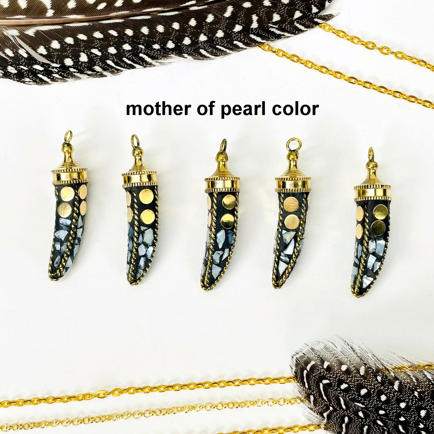 overhead view of five mother of pearl color petite mosaic horn pendants in a row on white background with decorations for possible variations