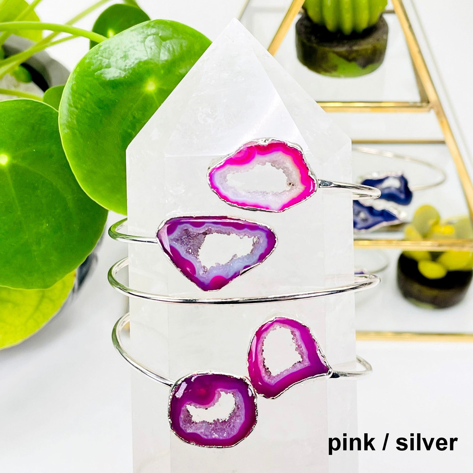 two pink / silver double agate adjustable bracelets facing forward and one facing backwards on a crystal quartz point in front of background decorations