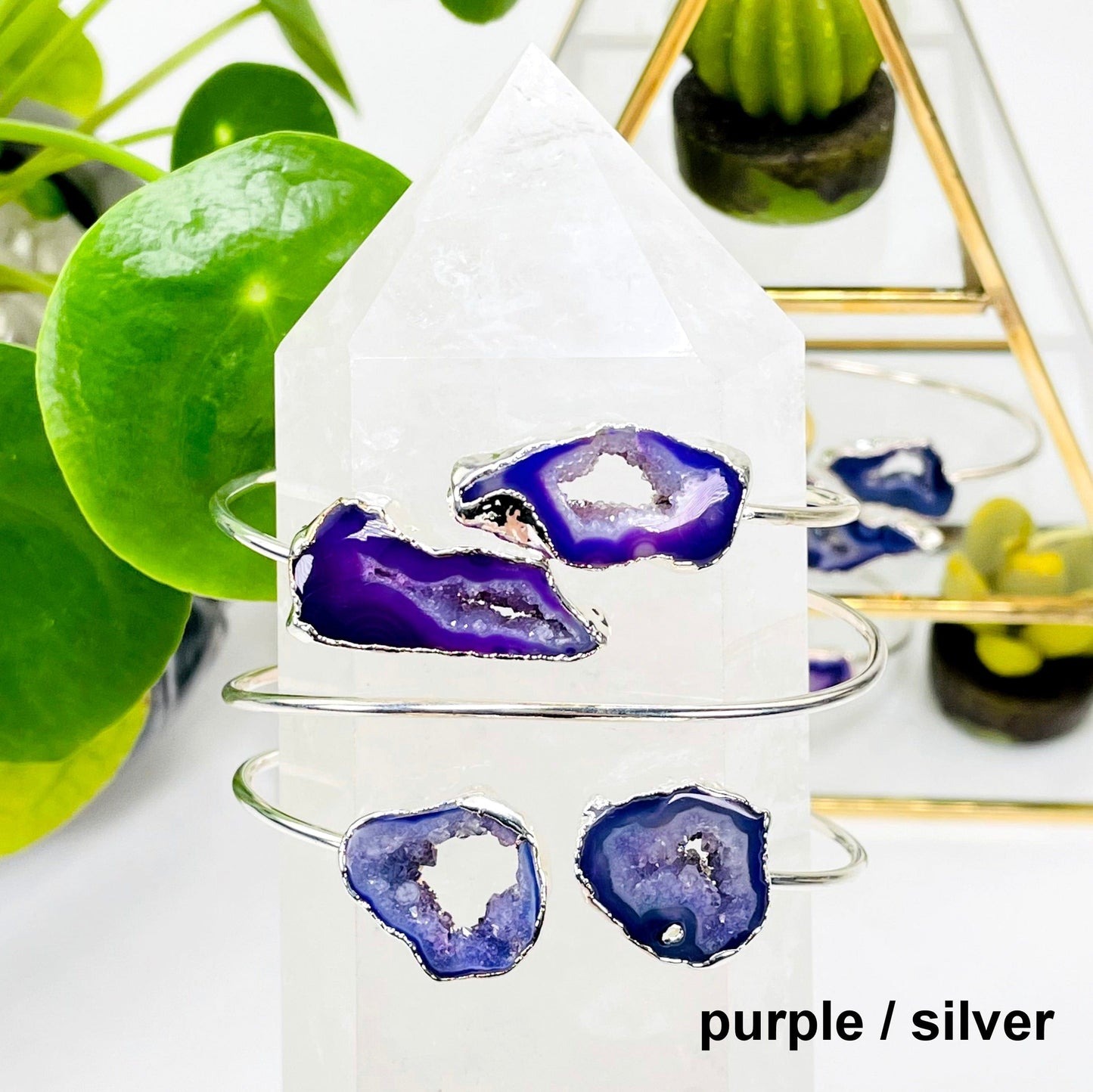 two purple / silver double agate adjustable bracelets facing forward and one facing backwards on a crystal quartz point in front of background decorations