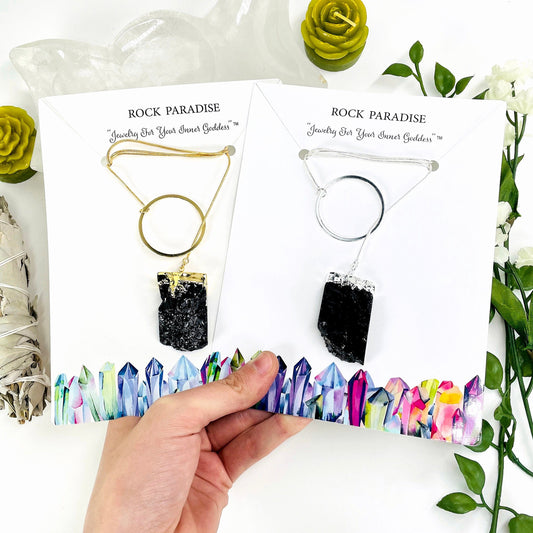 one gold and one silver obsidian chunk adjustable necklace in their packaging in hand for size reference and finish comparison