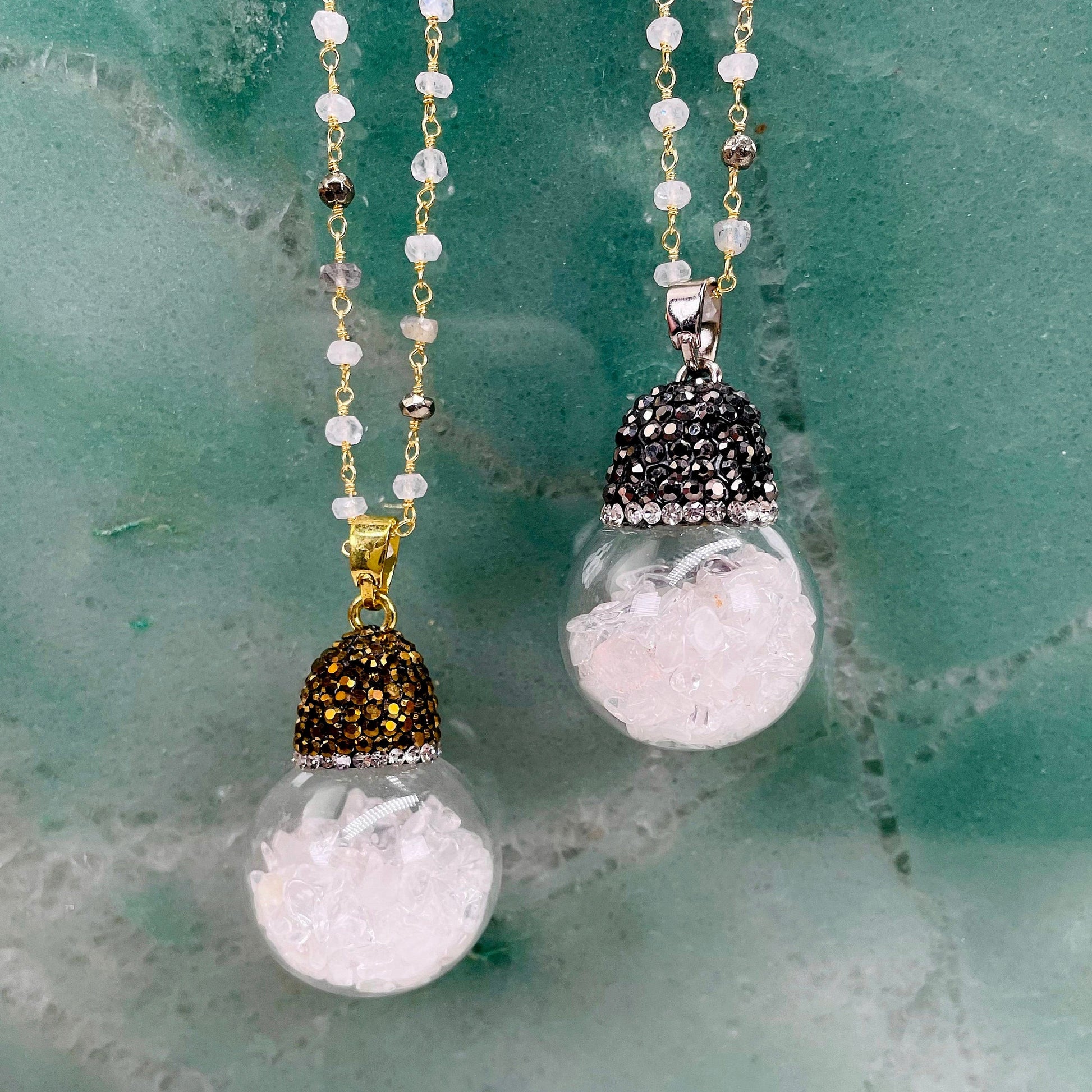 one gold and one silver glass sphere pendant necklace hanging on green background