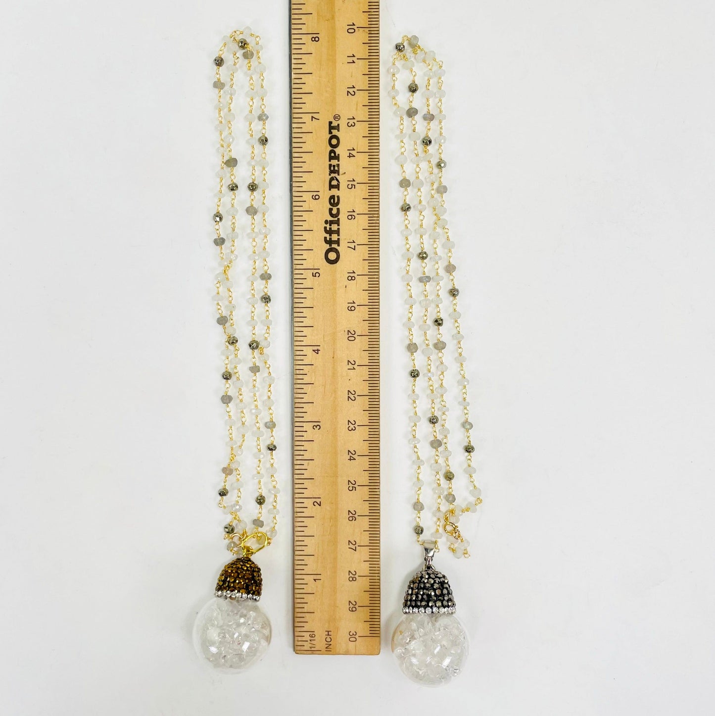 one gold and one silver glass sphere pendant necklace next to a ruler for length reference