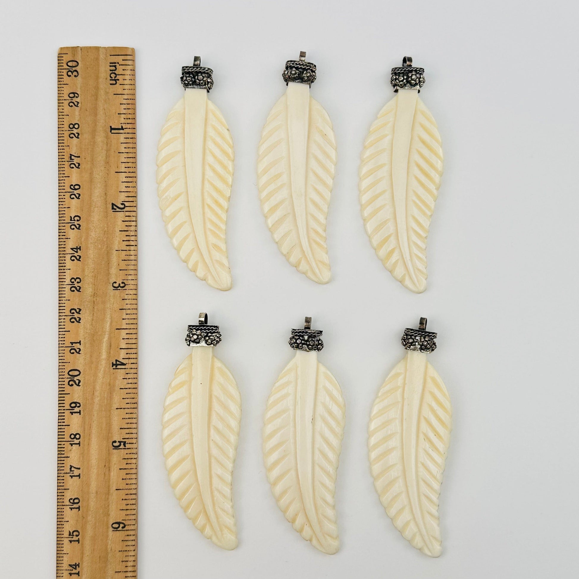 carved bone feather pendants next to a ruler for size reference 