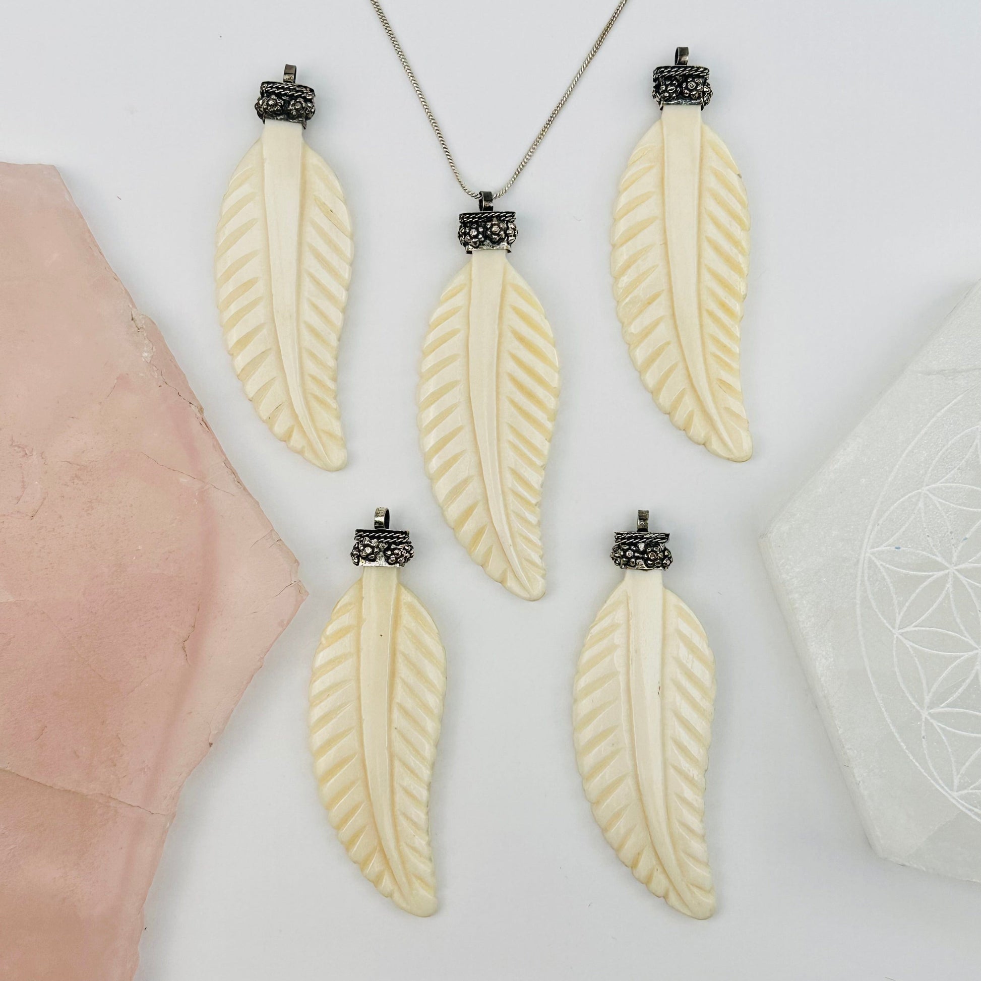 multiple carved bone feather pendants displayed to show the slight differences