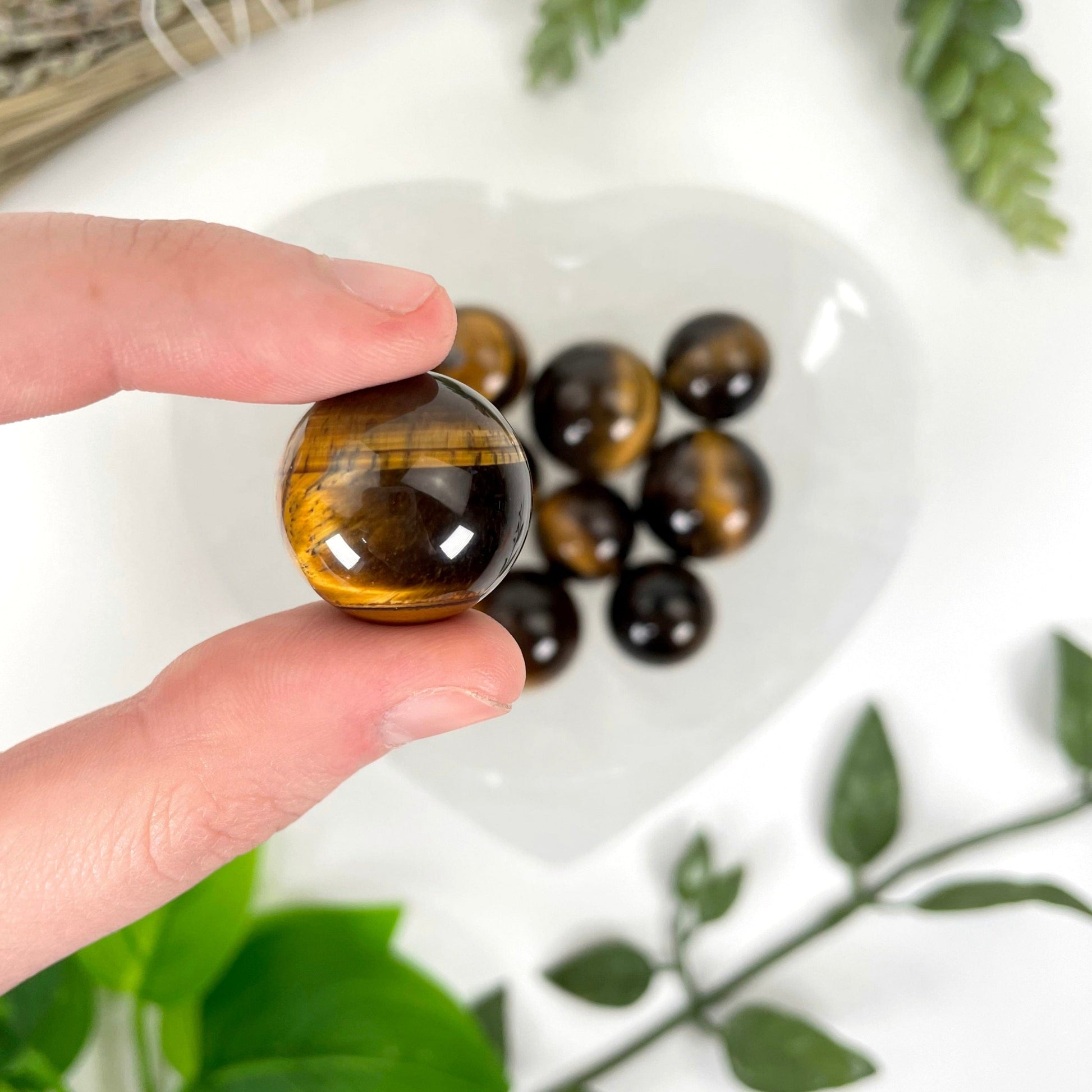 close up of one tigers eye sphere in hand for size reference with many others in a heart bowl in the background