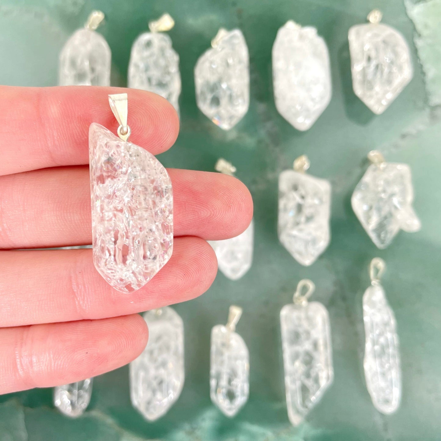 close up of one crackle quartz point pendant with silver bail in hand for size reference with many others in background