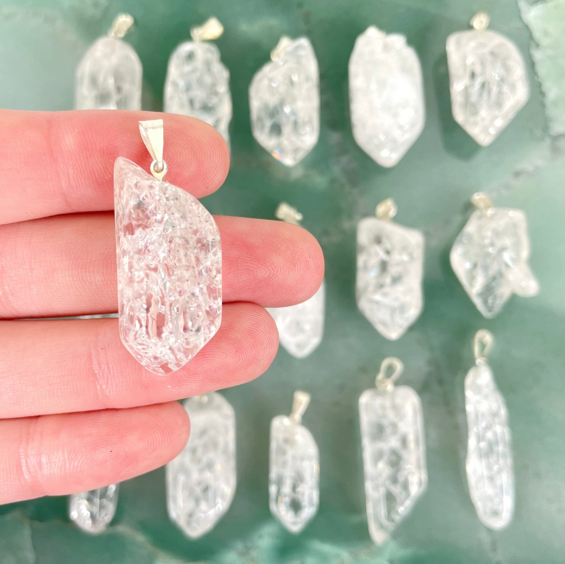close up of one crackle quartz point pendant with silver bail in hand for size reference with many others in background