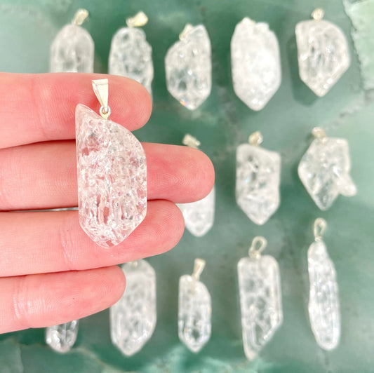 close up of one crackle quartz point pendant with silver bail in hand for size reference with many others in background