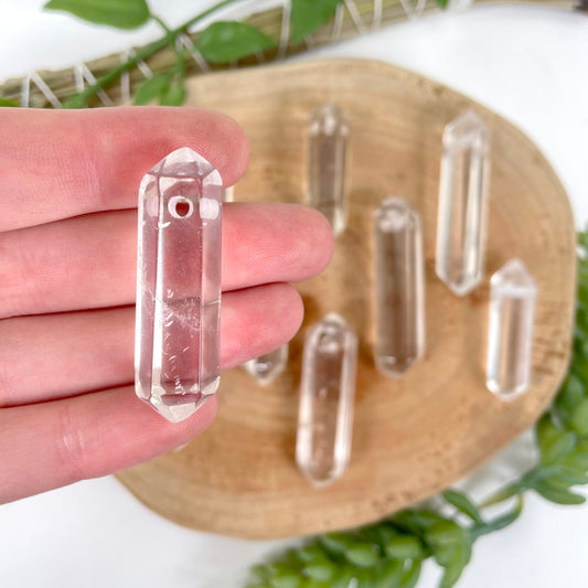 close up of one drilled crystal quart double point in hand for size reference and details with many others in background display