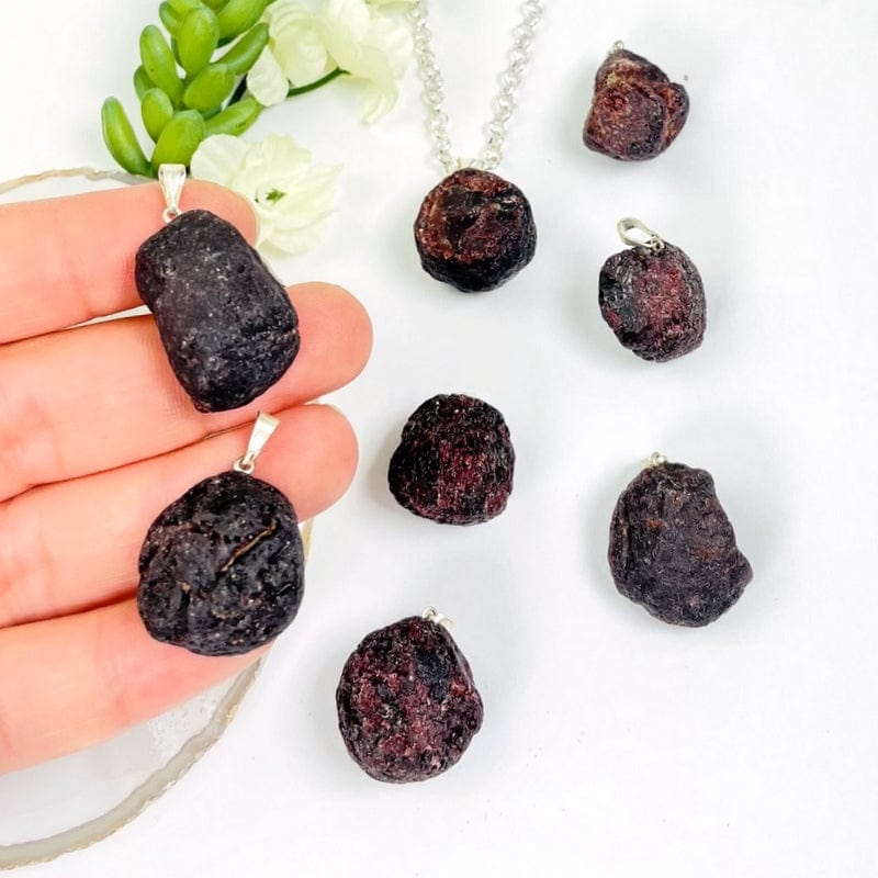 rough garnet pendant in a hand and on a table