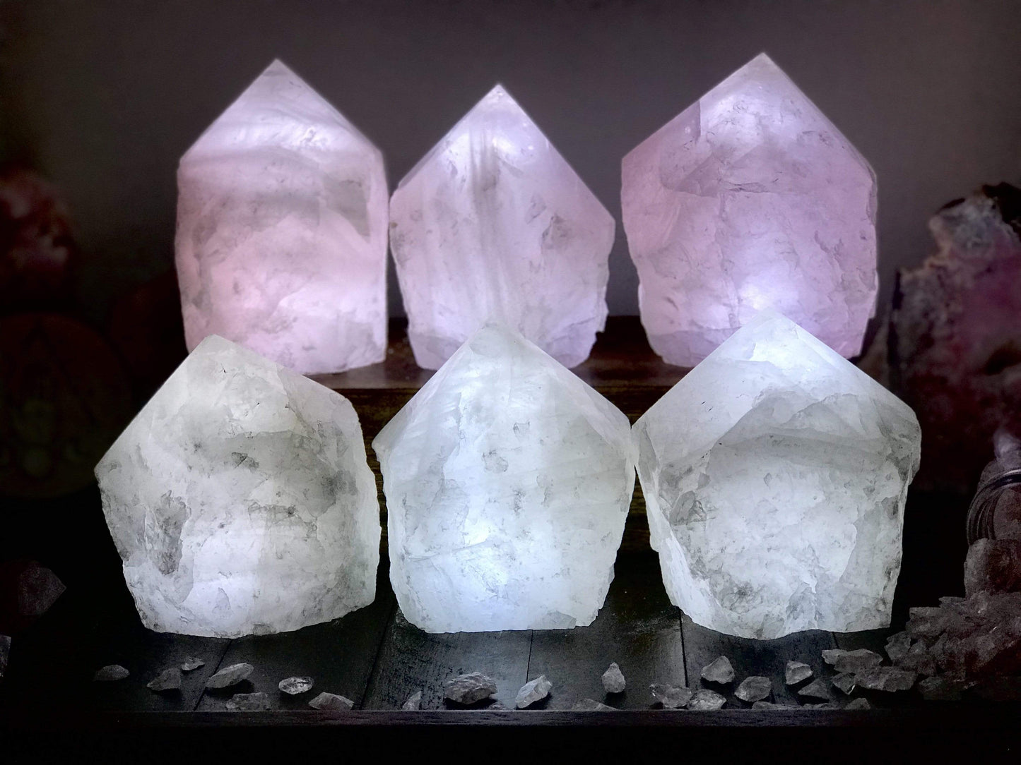 6 Rose Quartz and Crystal Lamps lit up in a dark room with other crystals as decoration