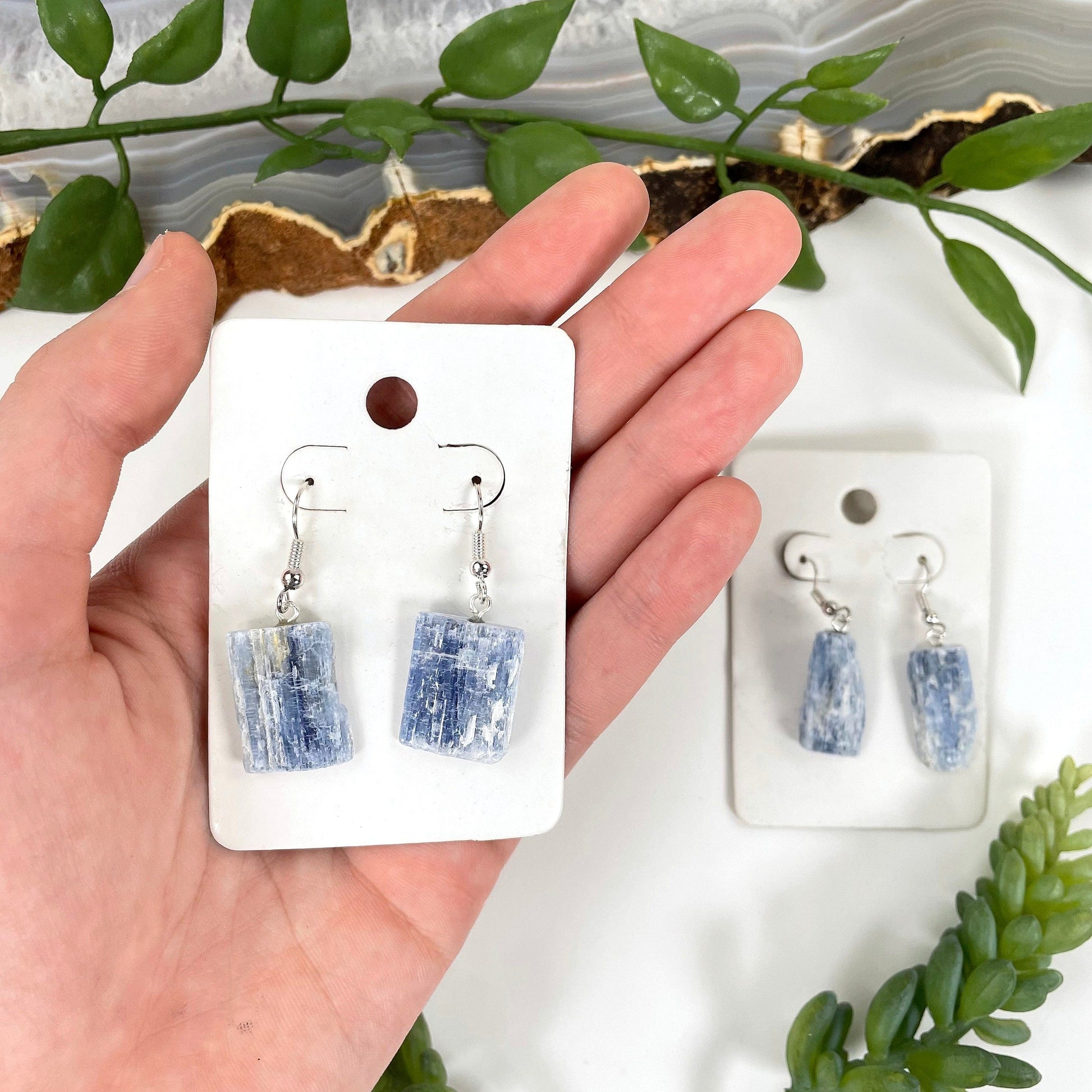 one pair of blue kyanite earrings in hand for size reference with one other in the background 