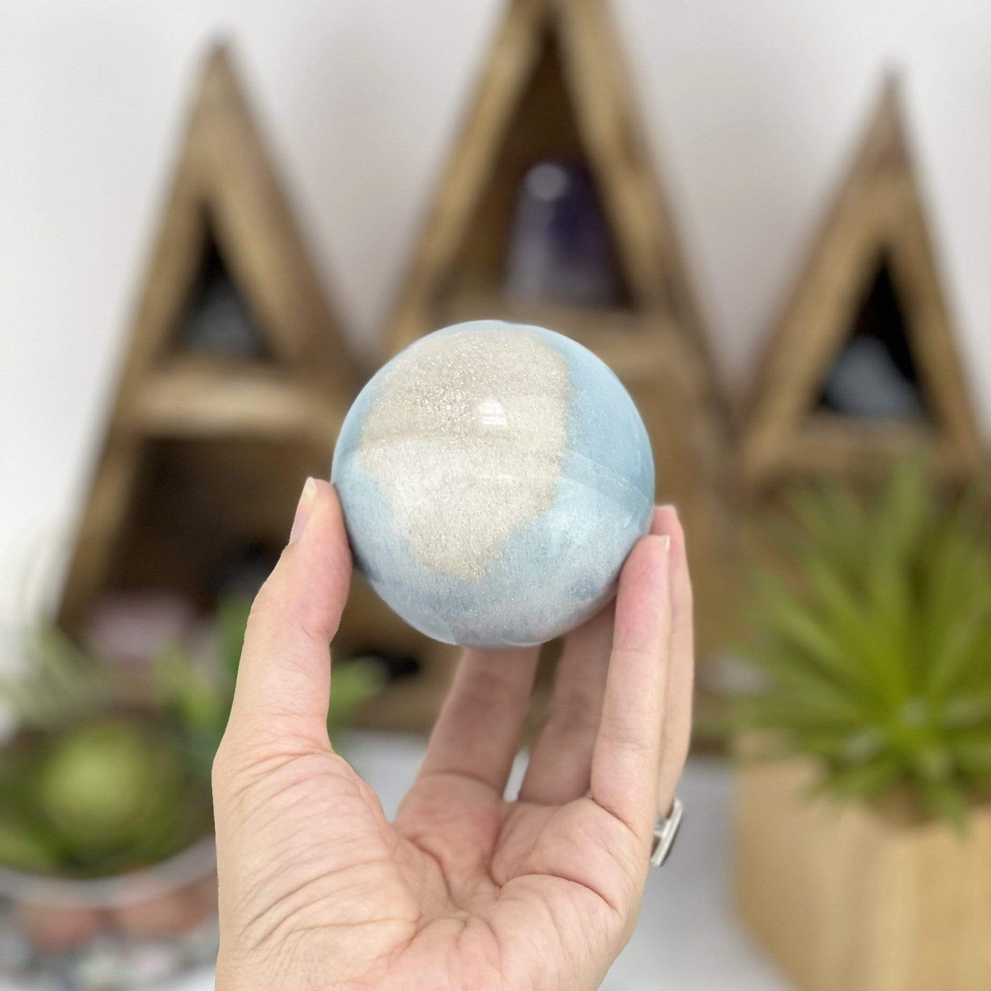 hand holding up Trolleite Sphere with decorations in the background