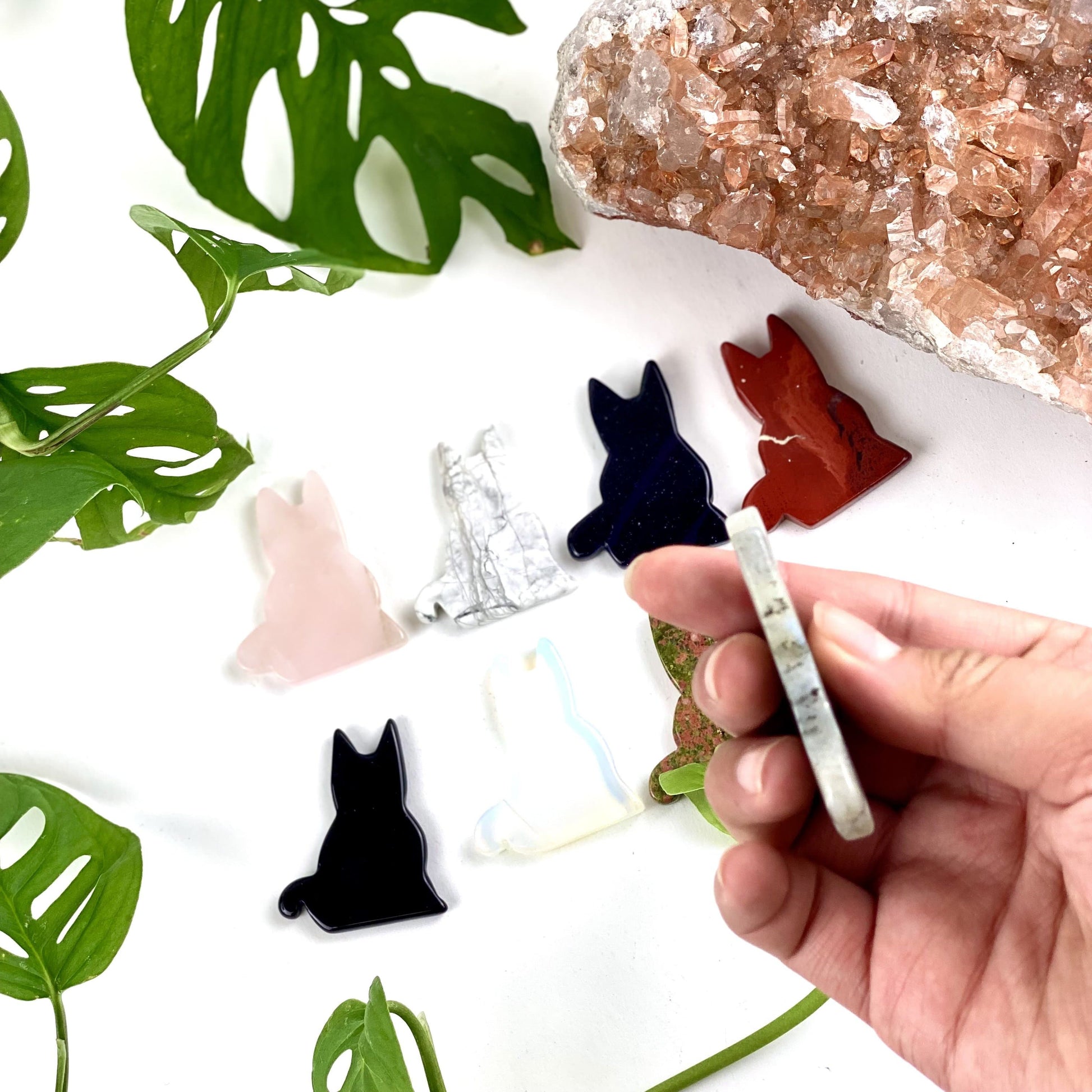 side view of labradorite cat crystal figurine in hand with other cat crystals in the background with a white backdrop