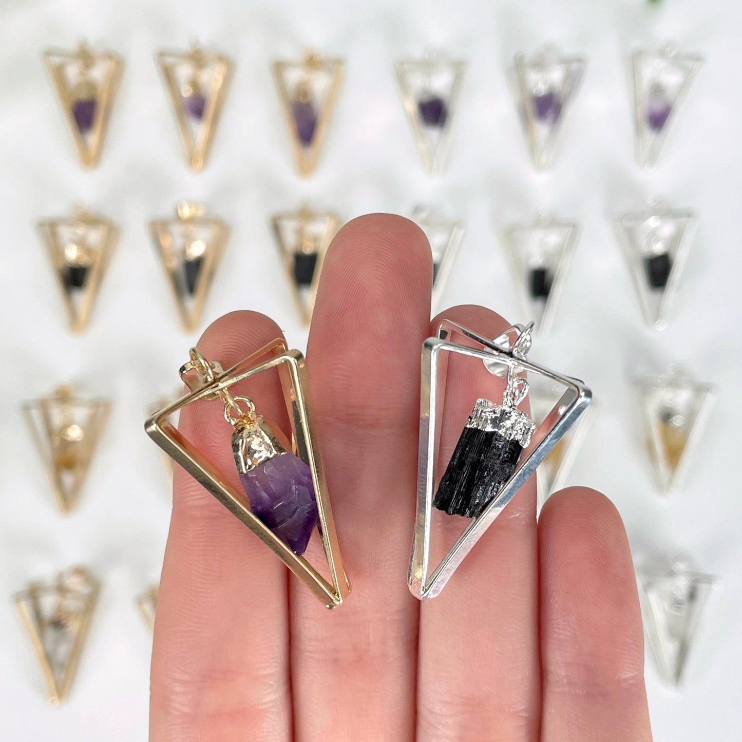 close up of two dangle stone point pendulum pendants in hand for size reference and possible variations with many others in the background