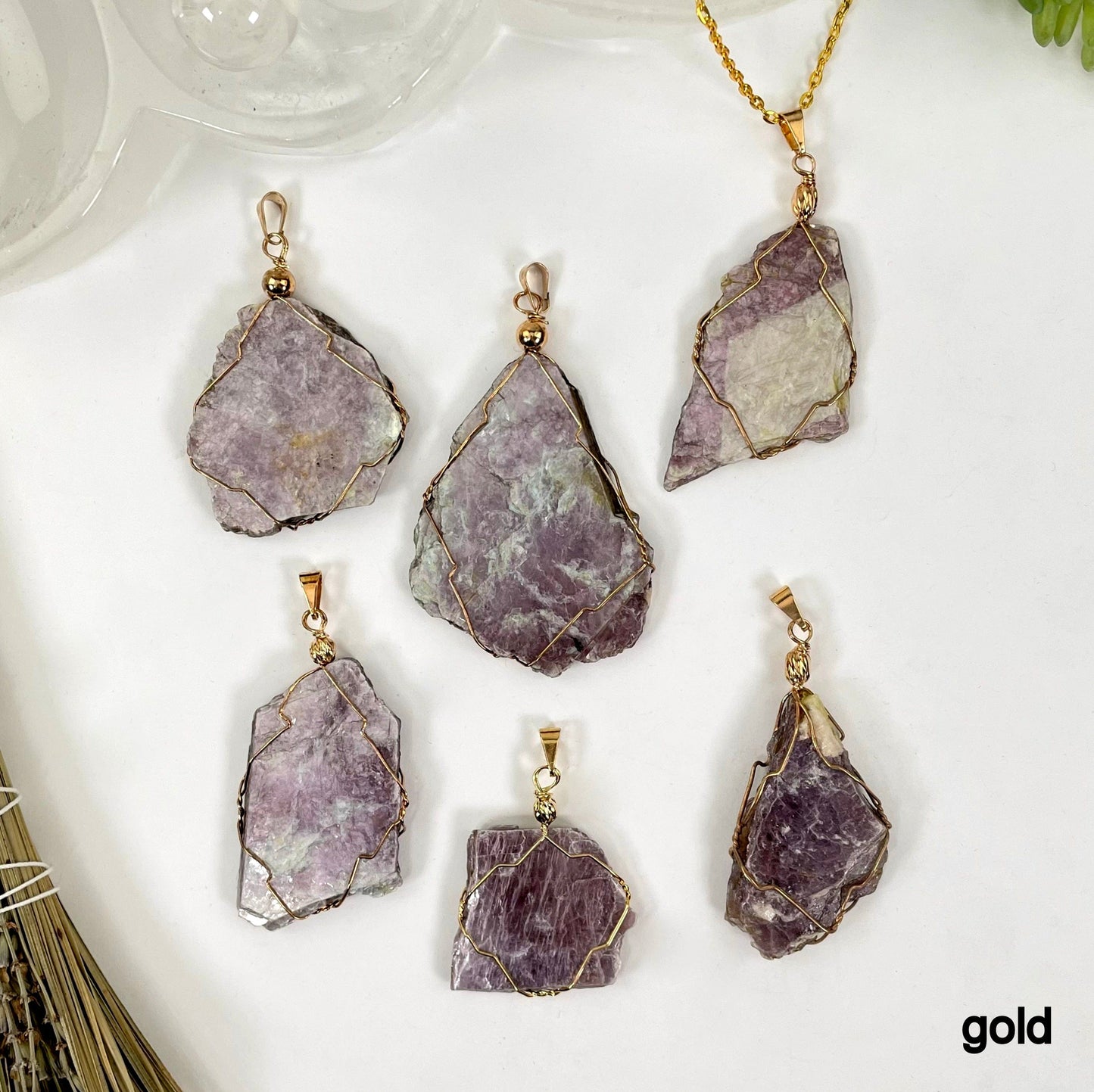 overhead view of six gold purple mica wire wrapped pendants on white background with one strung on gold chain for possible variations