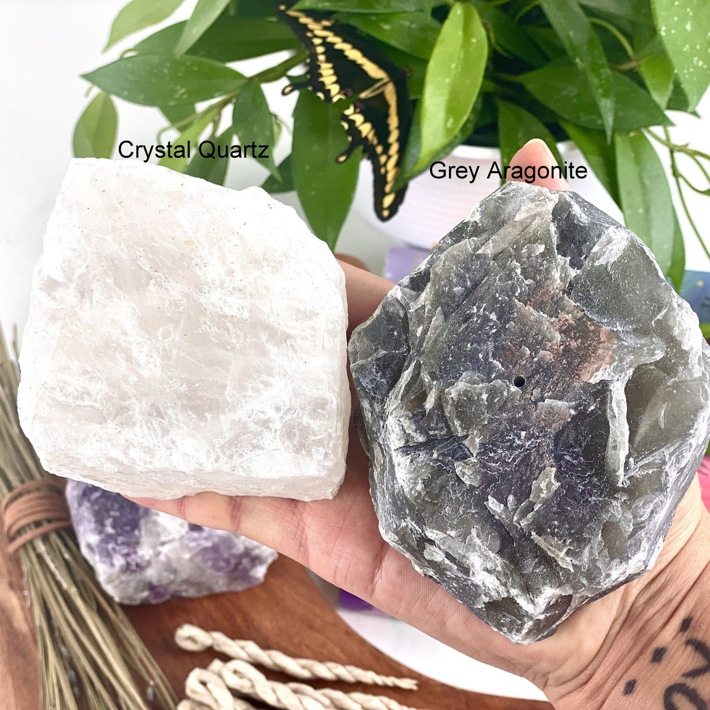 Hand holding 1 crystal quartz and 1 grey aragonite Rough Stone Incense Burner with decorations in the background