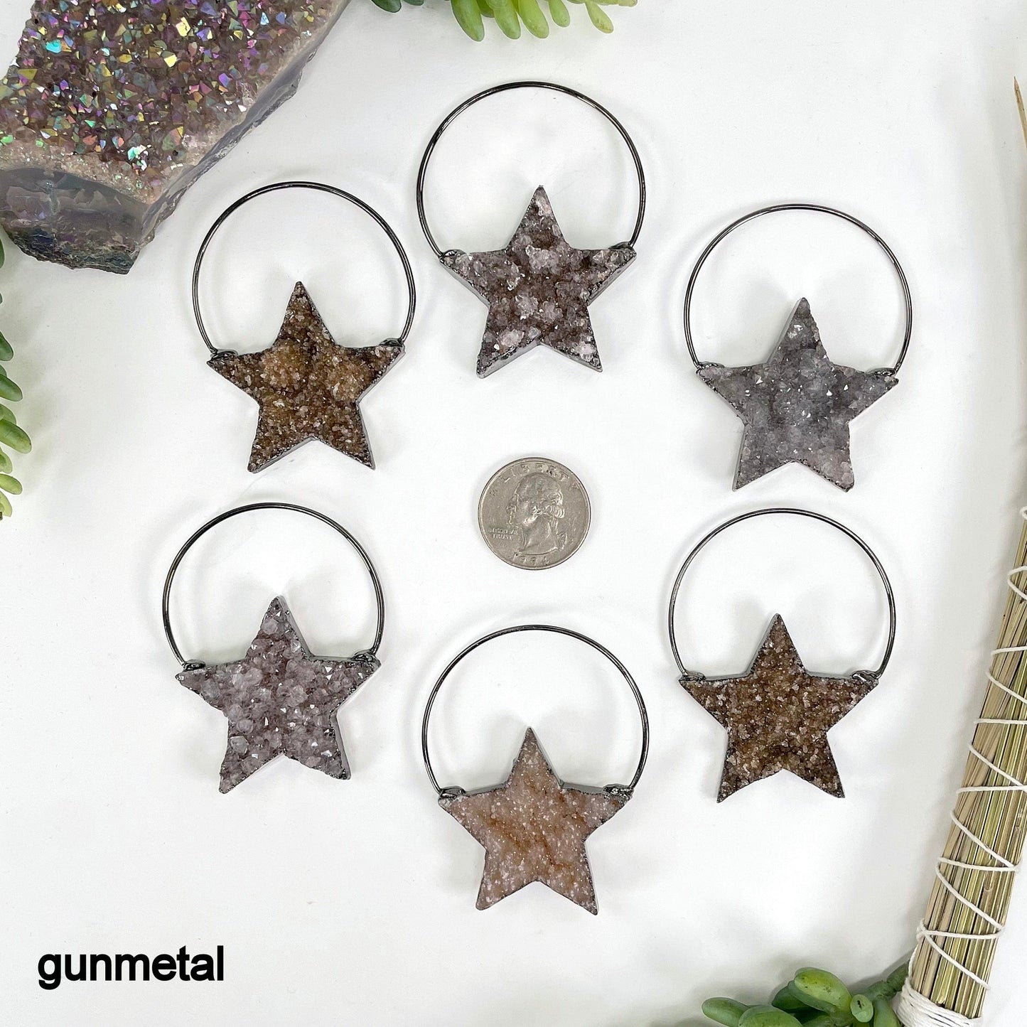 overhead view of six gunmetal druzy star pendants on white background with a quarter for size reference