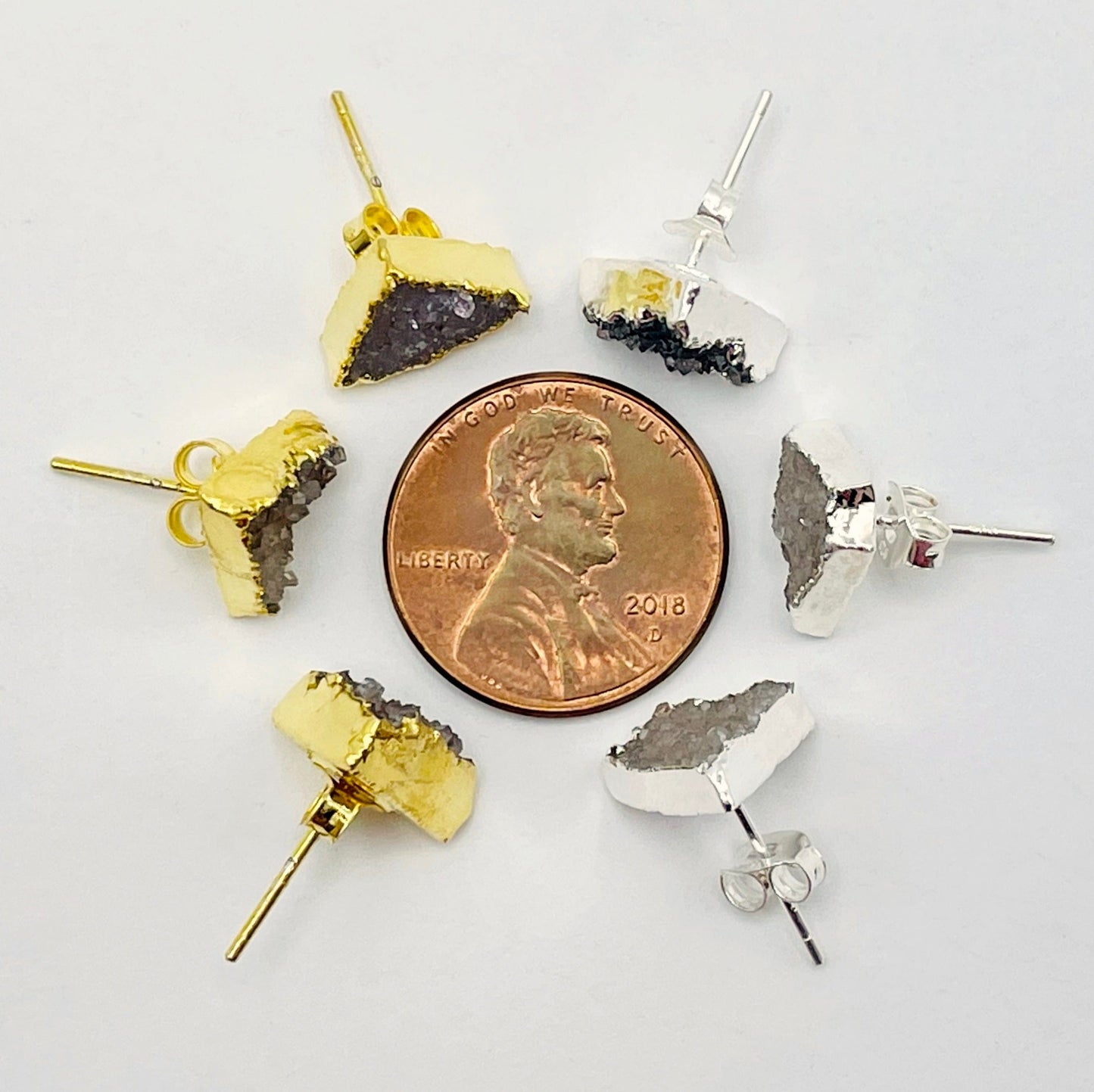 overhead view of three gold and three silver natural druzy triangle stud earrings surrounding a penny for size reference