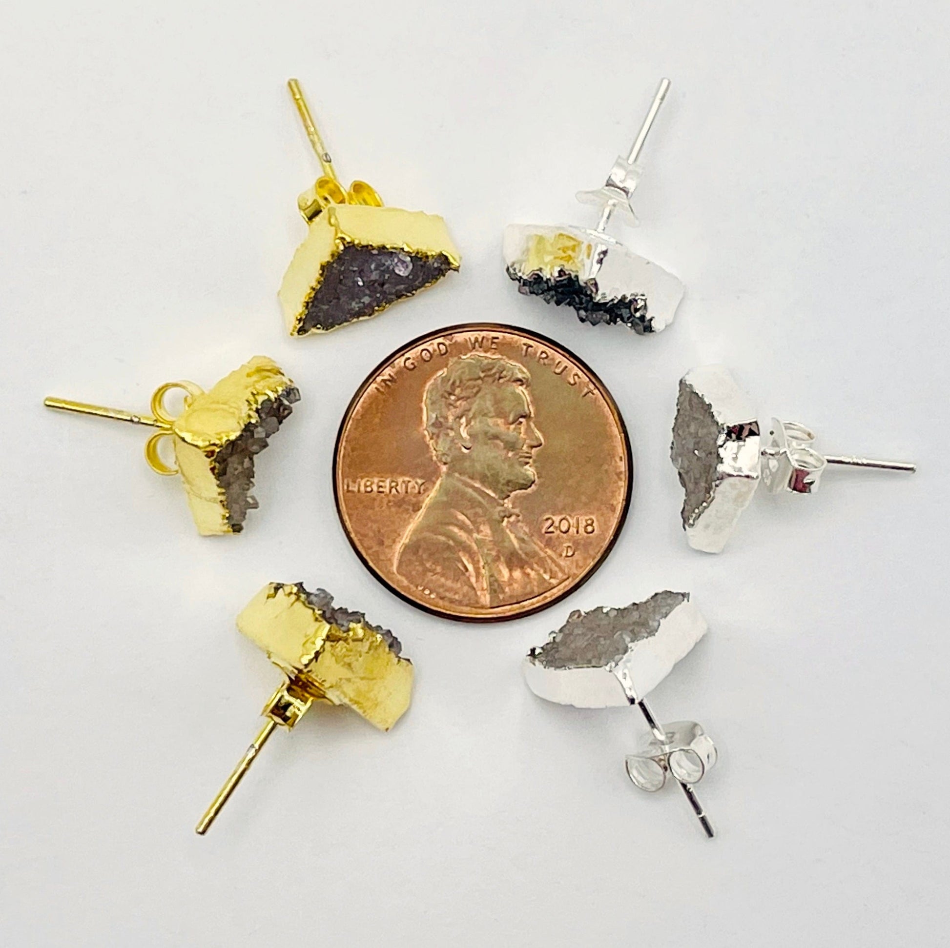 overhead view of three gold and three silver natural druzy triangle stud earrings surrounding a penny for size reference