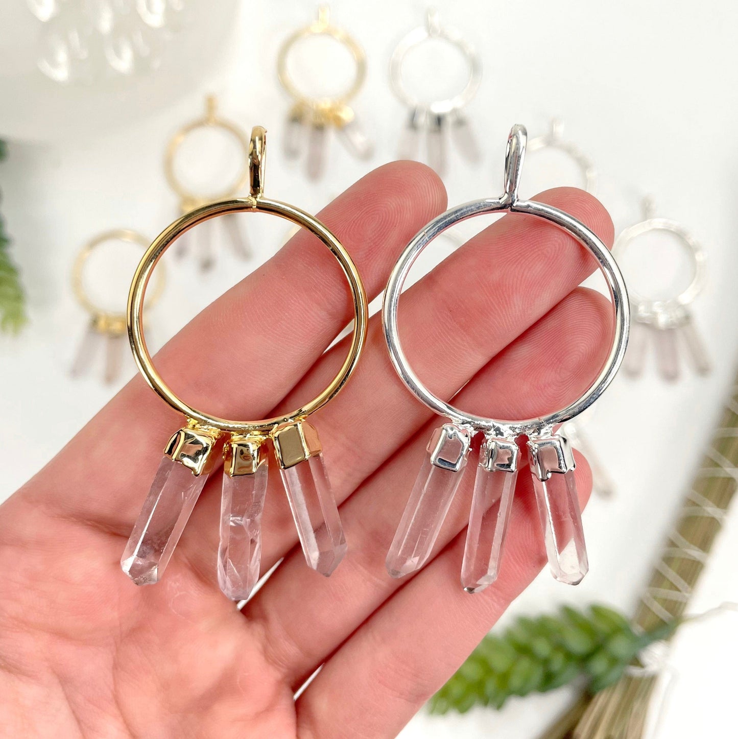 close up of one gold and one silver triple crystal point pendant in hand for size reference and finish comparison