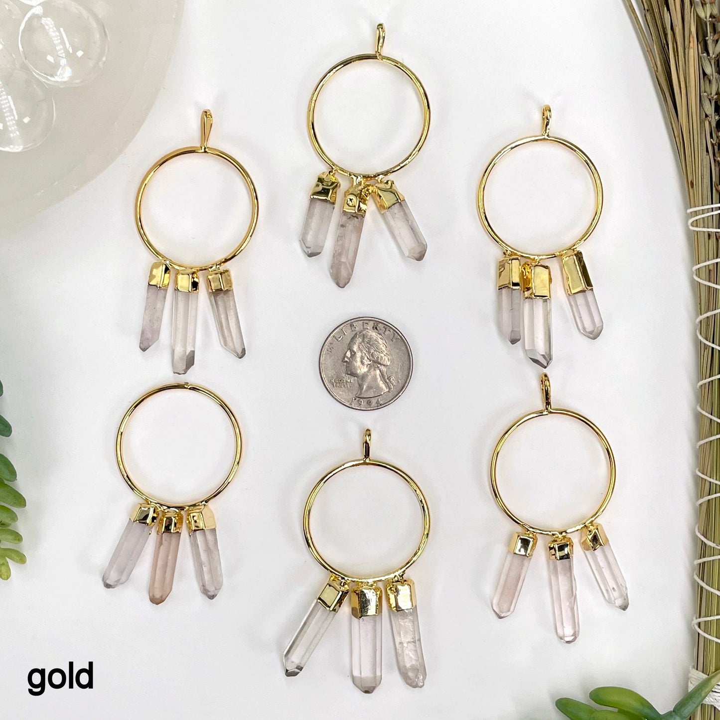 six gold triple crystal point pendants on white background with a quarter for size reference