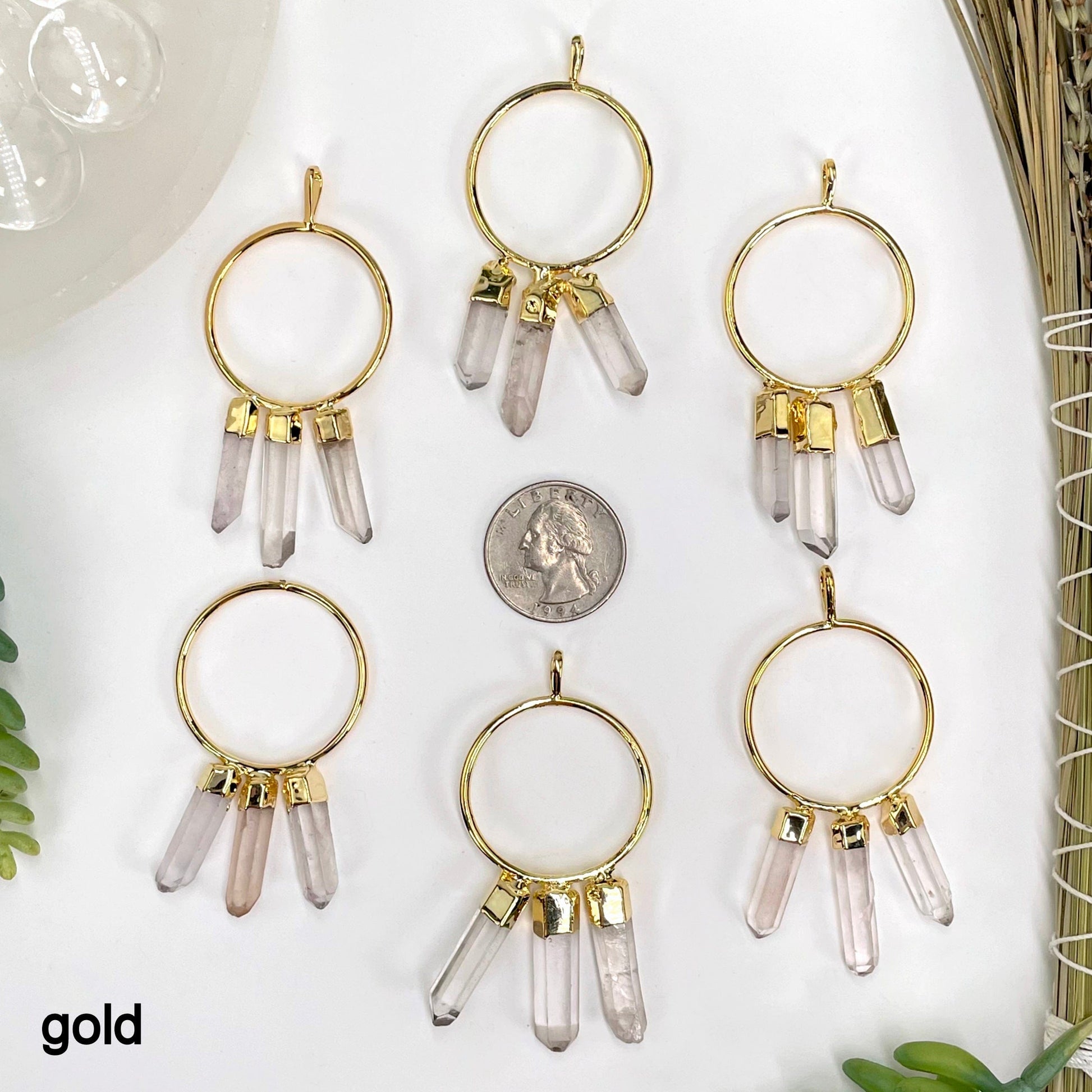 six gold triple crystal point pendants on white background with a quarter for size reference