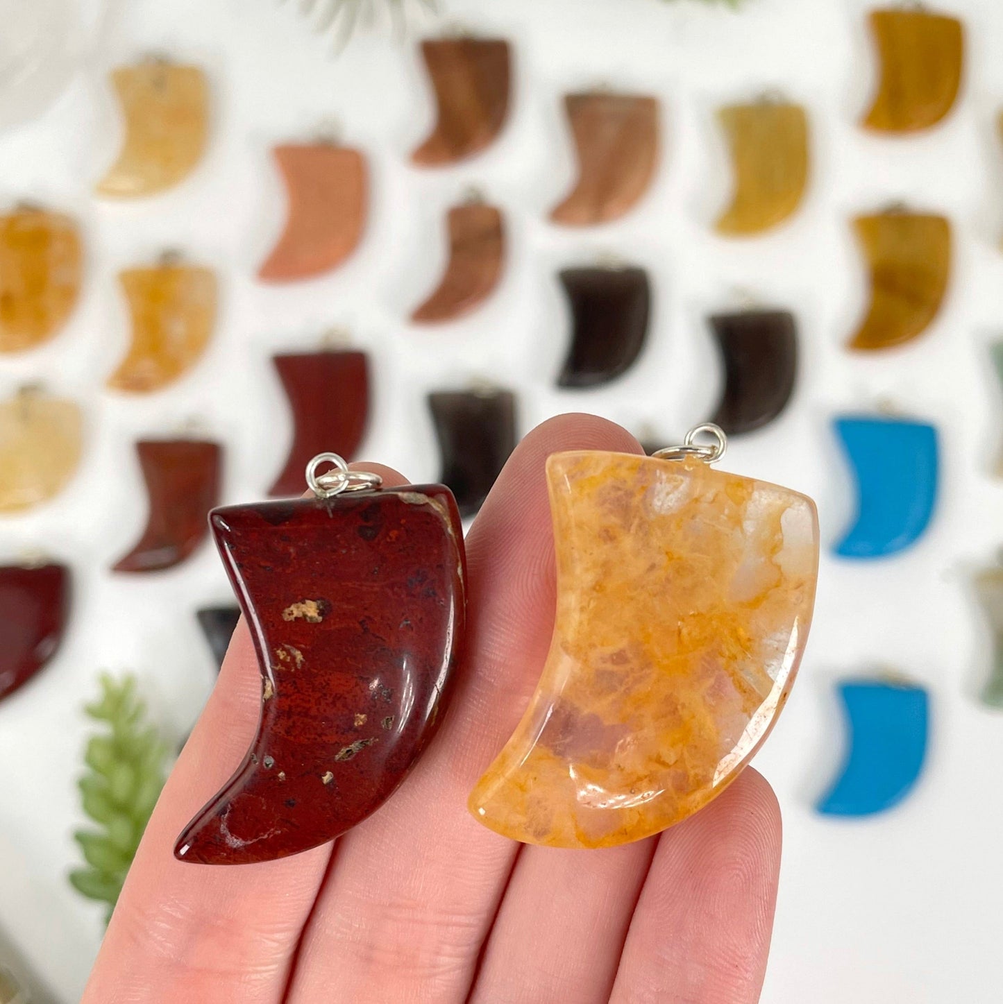 close up of two tumbled horn pendant options in hand for size reference with many others in the background