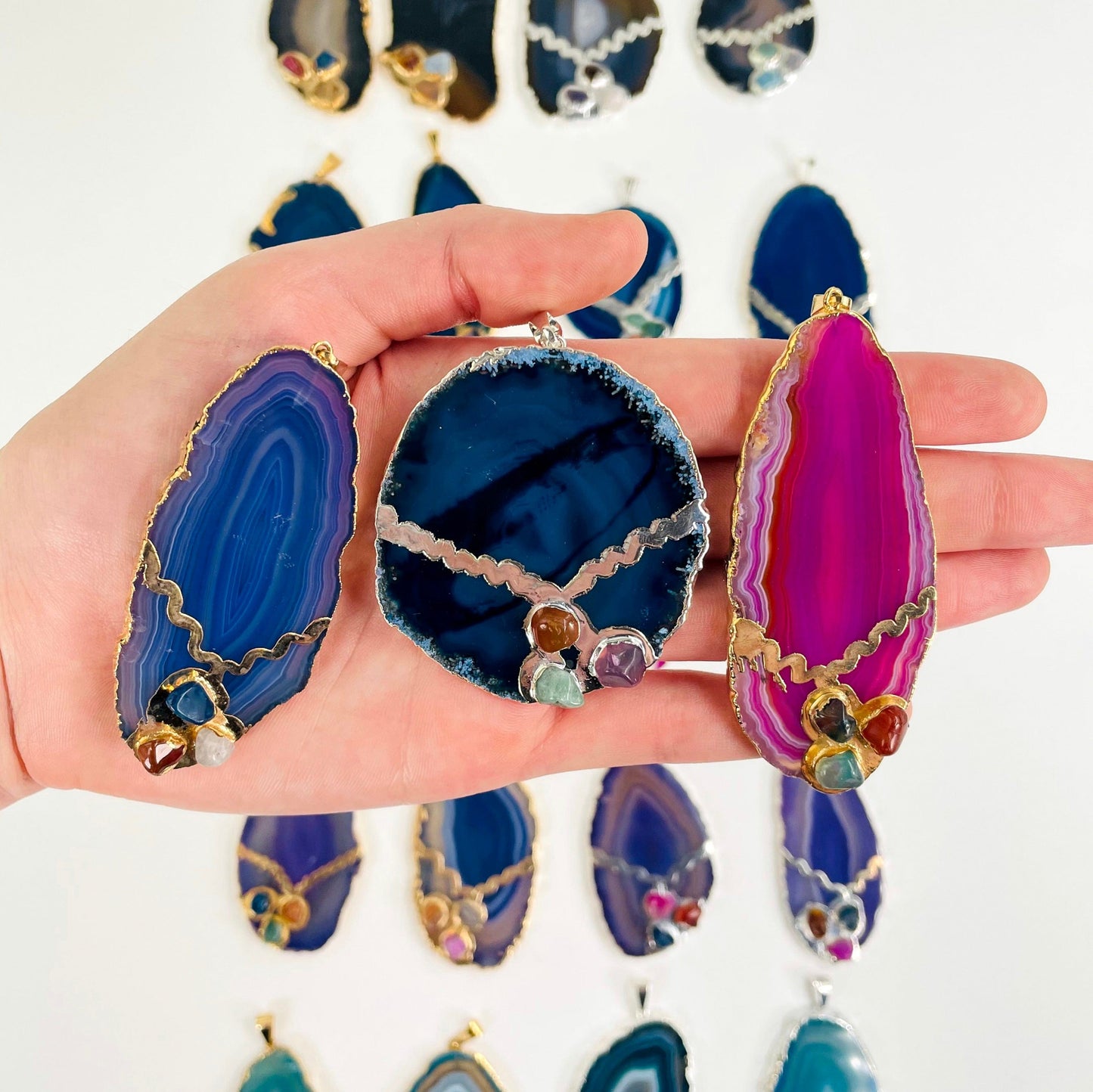 three different agate slice pendants in hand for size reference and possible options with many others in the background