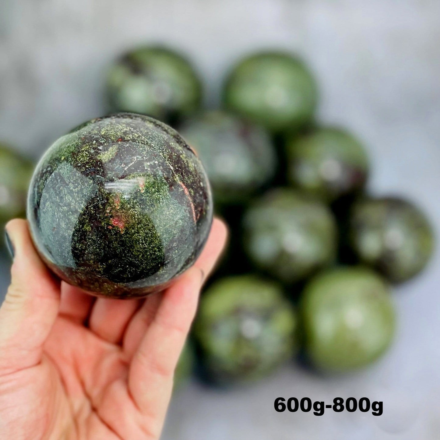 Dragon Blood Stone Sphere in Hand on Gray Background.