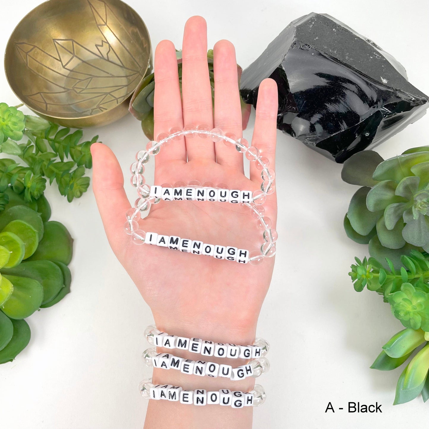 black "IAMENOUGH" letter bead in hand and on wrist for color reference