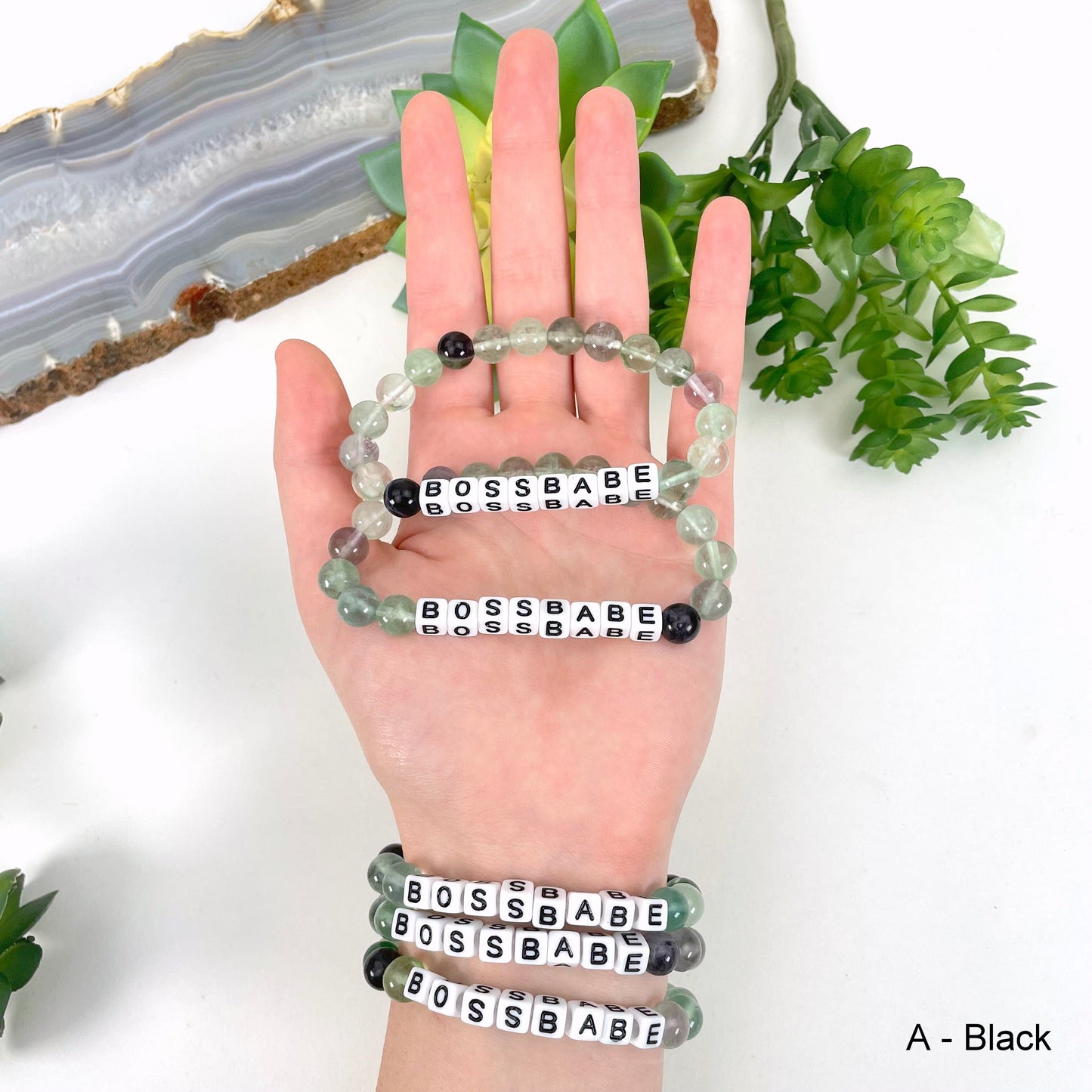Fluorite round bead with black print on white bead"BOSSBABE" letter bead option in hand and on wrist for color reference