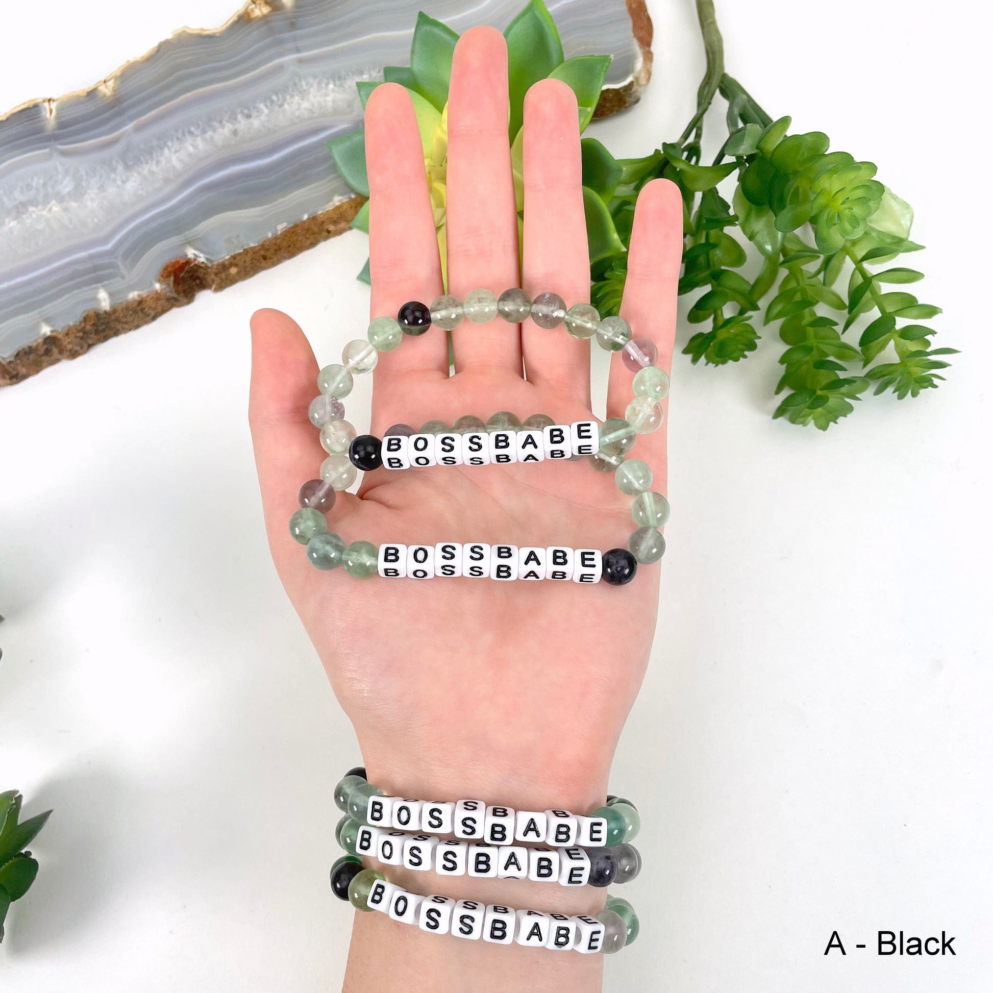 Fluorite round bead with black print on white bead"BOSSBABE" letter bead option in hand and on wrist for color reference