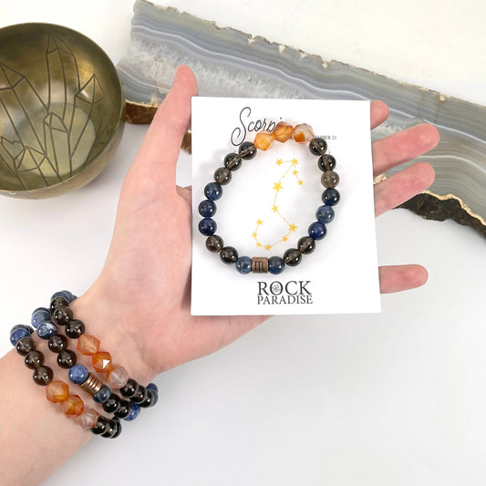 packaged scorpio zodiac bracelet in hand with scorpio zodiac bracelets on wrist