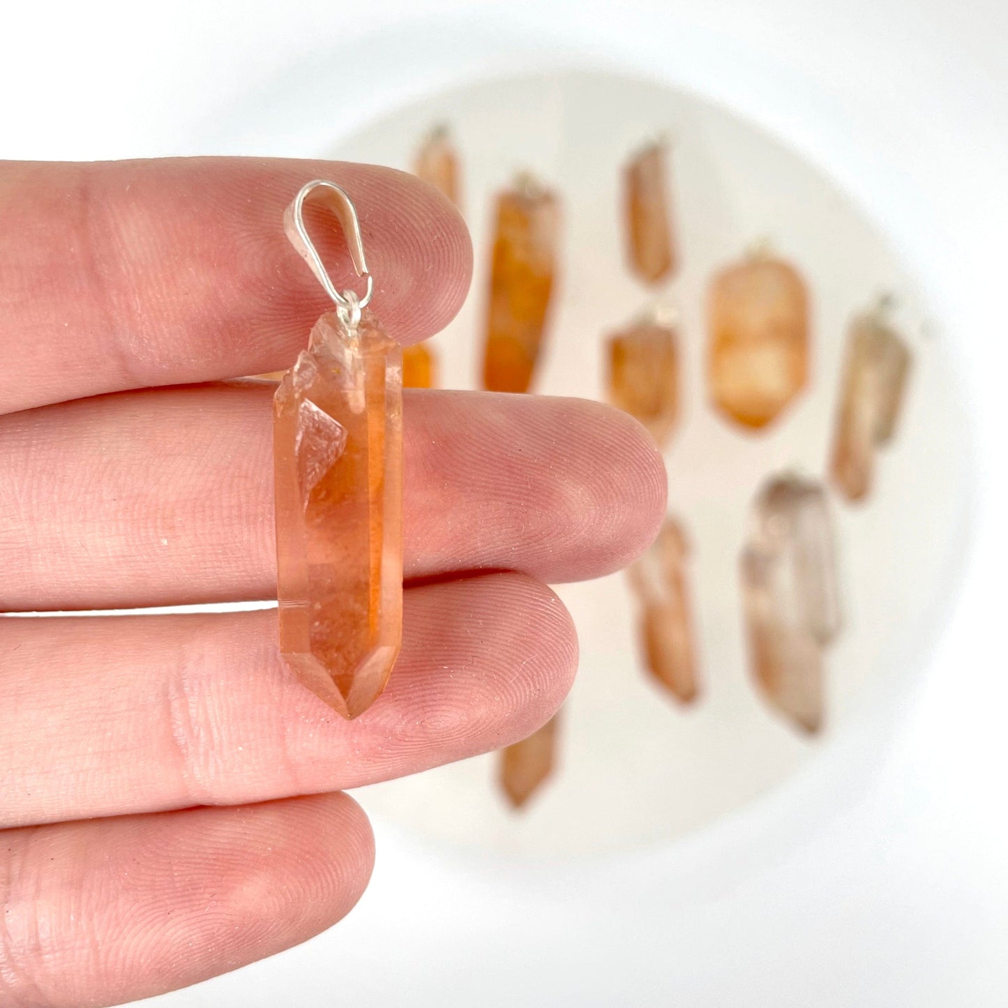 close up of one tangerine rough point pendant in hand for size reference with many others in background