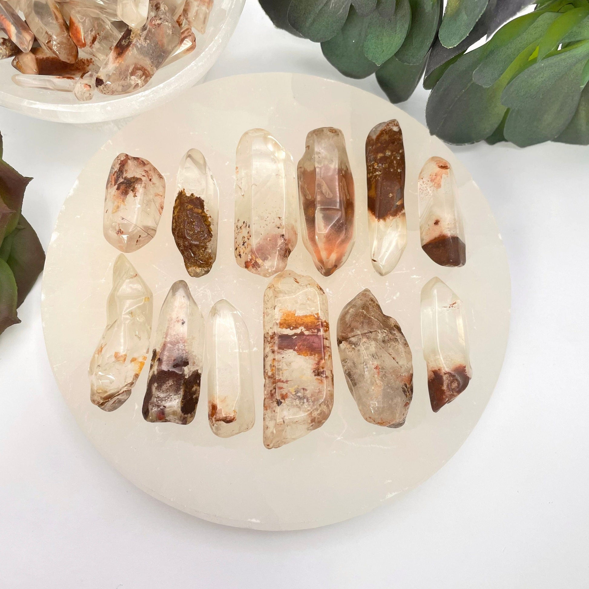 many large tumbled quartz with hematite points on display for possible variations