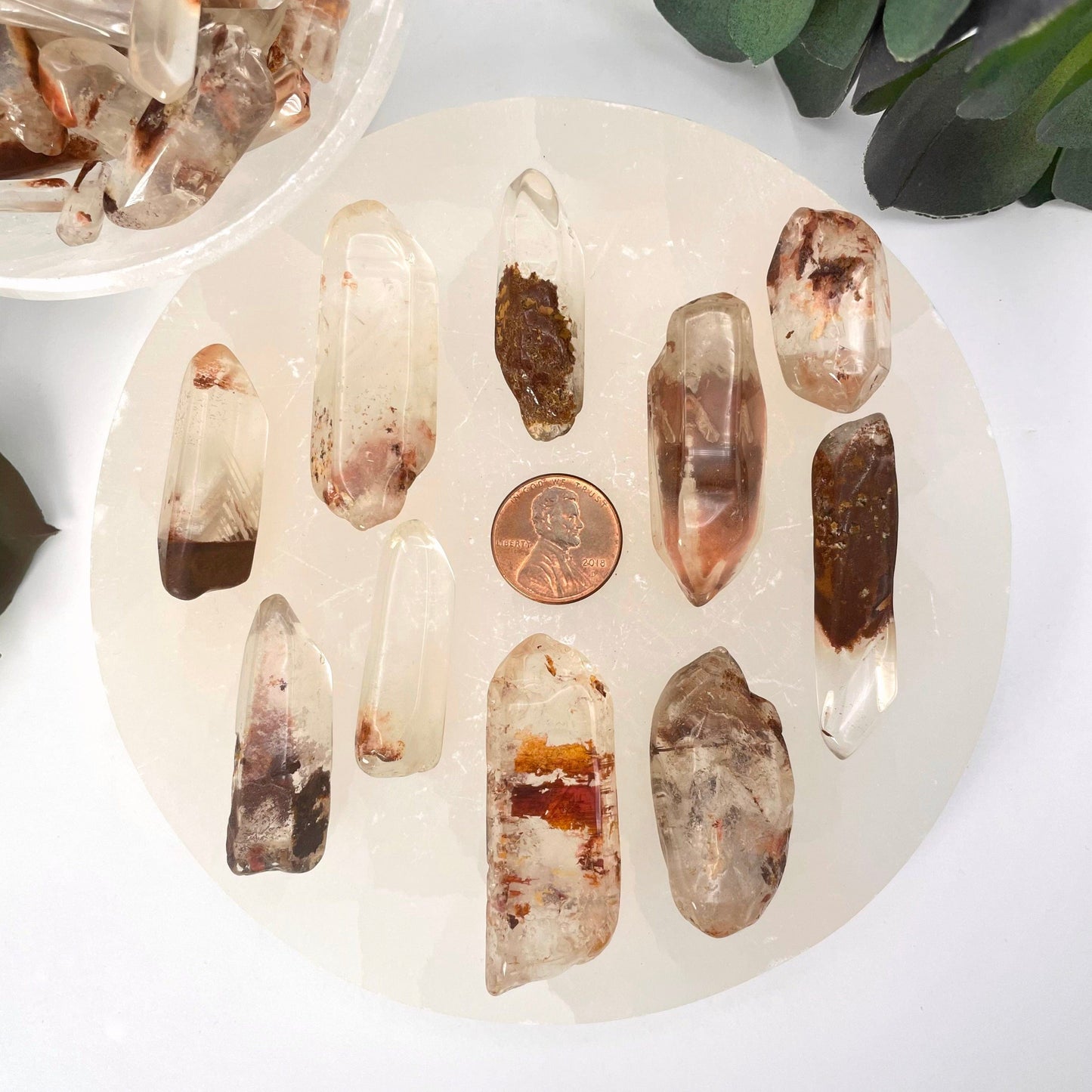many large tumbled quartz with hematite points on display with penny for size reference