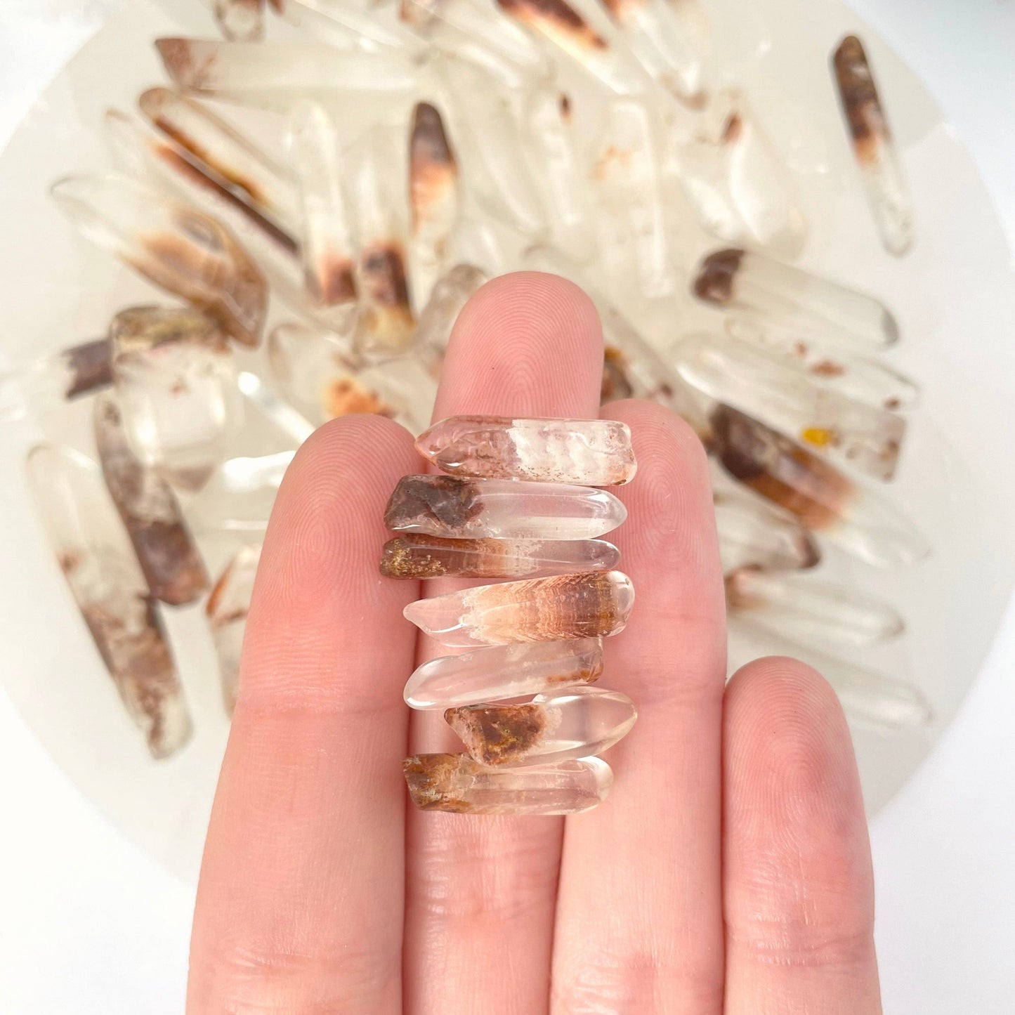 seven small tumbled quartz with hematite points in hand in front of backdrop for size reference and possible variations
