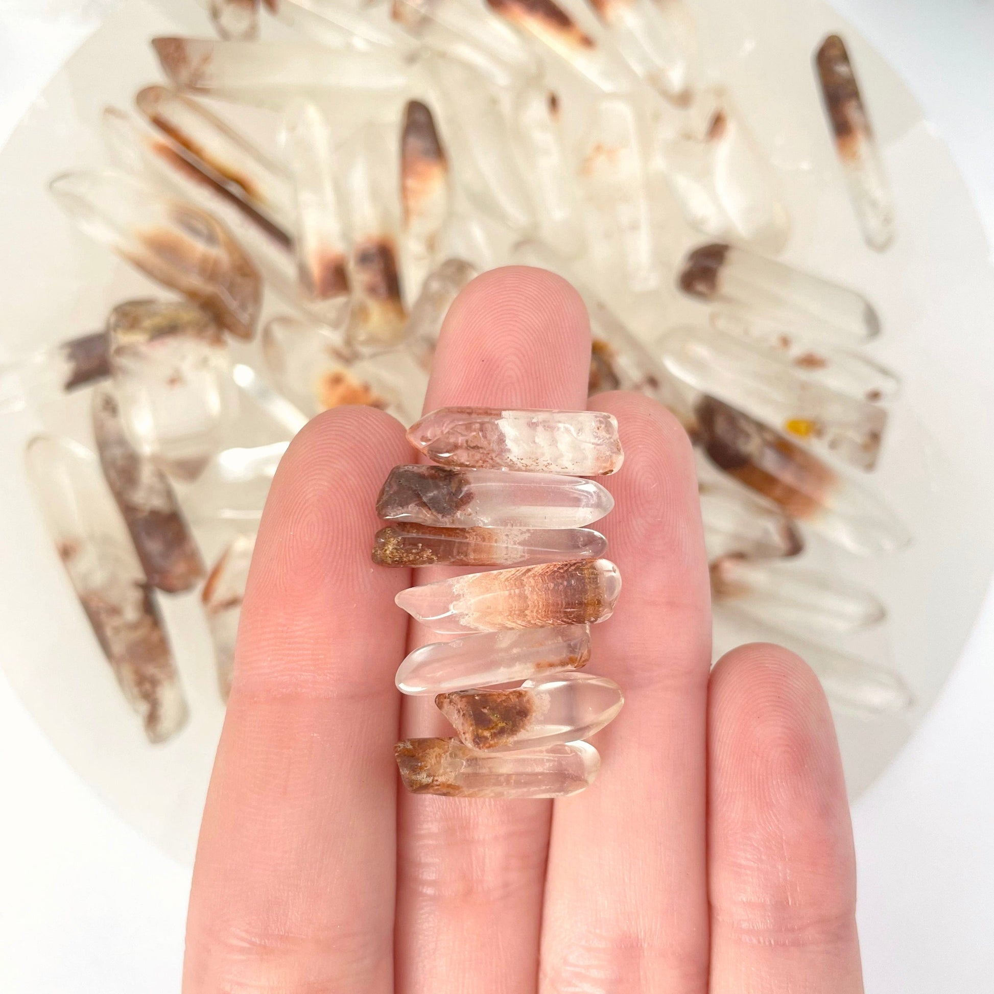 seven small tumbled quartz with hematite points in hand in front of backdrop for size reference and possible variations