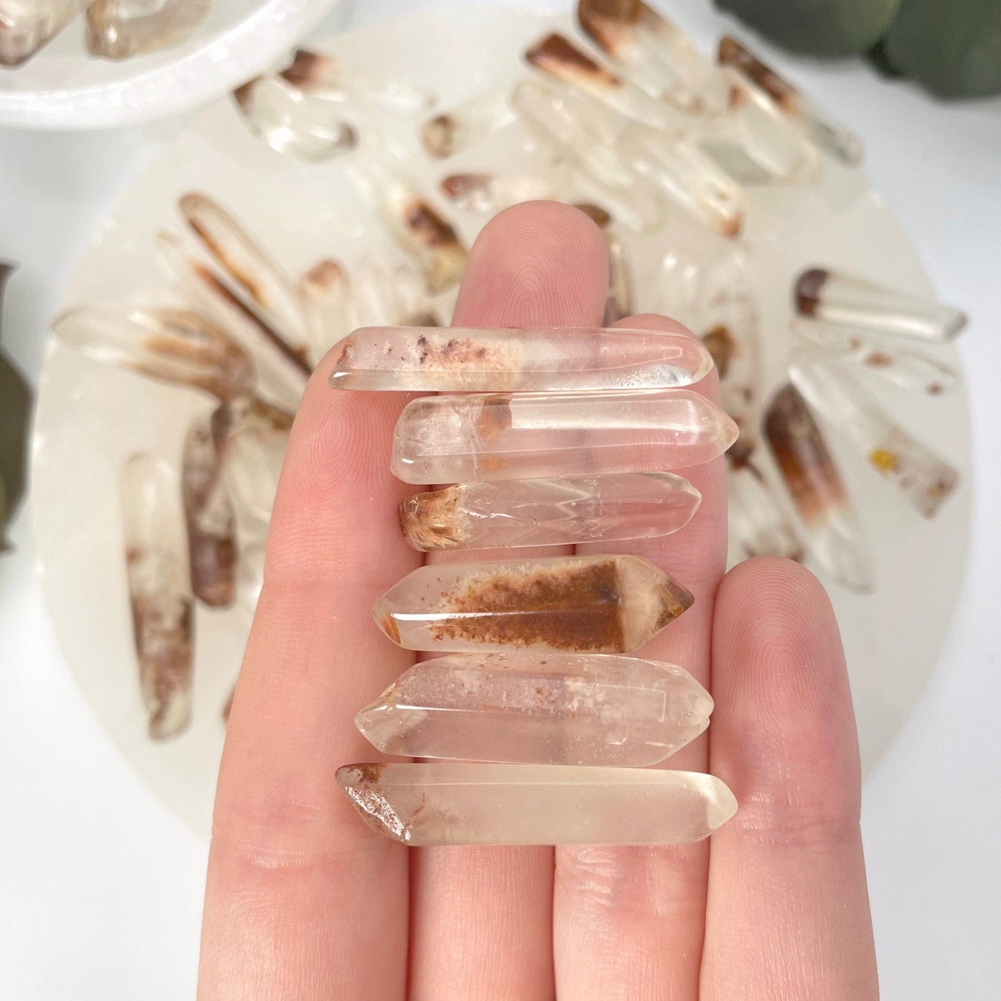 six large tumbled quartz with hematite points in hand in front of backdrop for size reference and possible variations