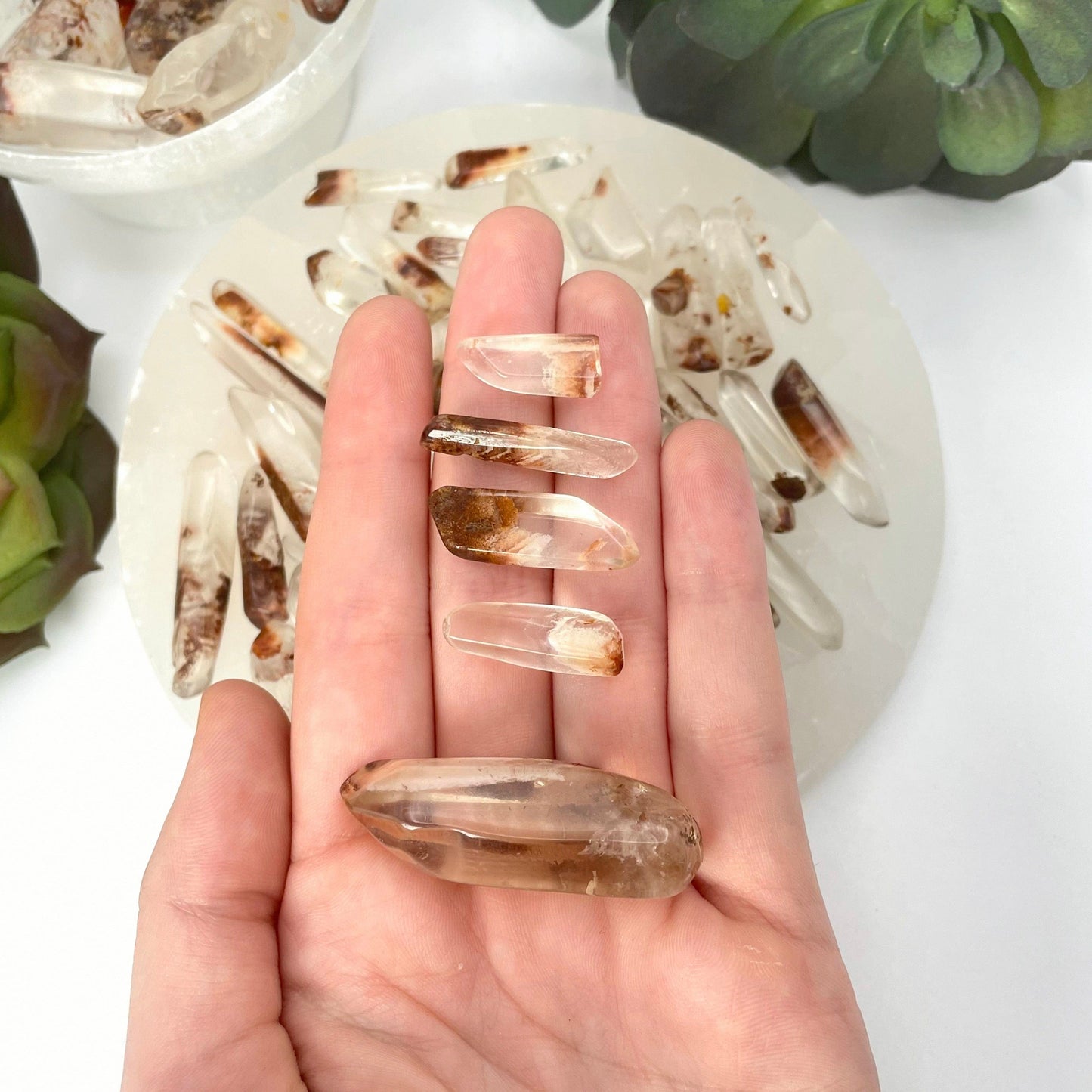 tumbled quartz with hematite points set of five (one large, four small) in hand in front of backdrop for size reference