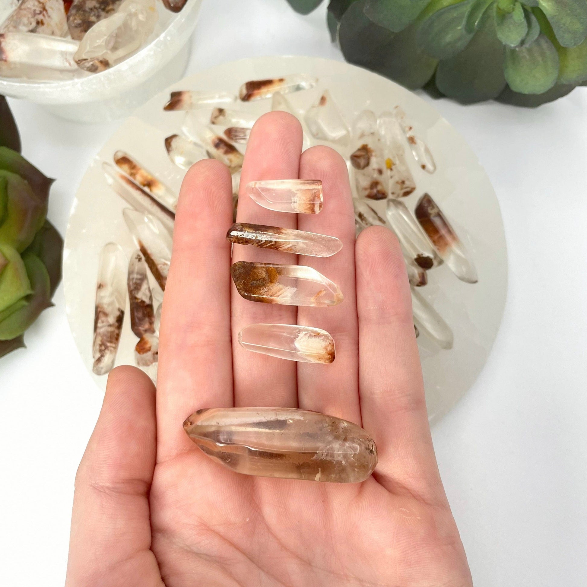 tumbled quartz with hematite points set of five (one large, four small) in hand in front of backdrop for size reference