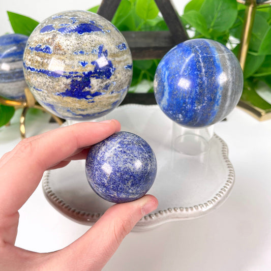 three different lapis lazuli polished sphere weights on display with hand on one 
