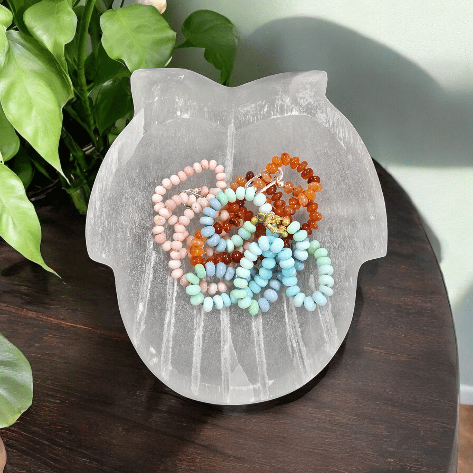 Selenite Hands Crystal Bowl top view with jewelry in hands bowl with plants and wooden table in the background